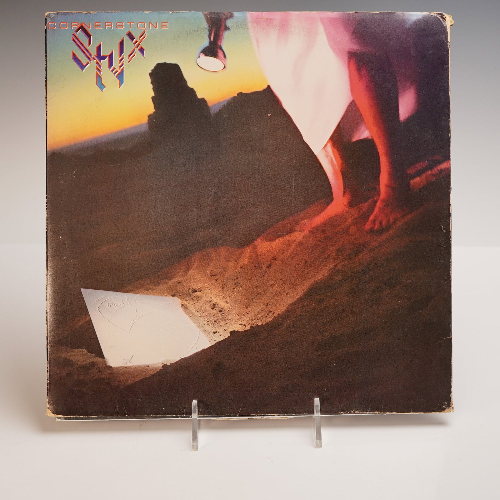 Styx Vinyl Record, Cornerstone: A vibrant vinyl of Styx Cornerstone, pressed on black vinyl with a soft beige A&M label. The front cover features glowing sand tones with a mysterious carved stone lit by a flashlight. The back cover 