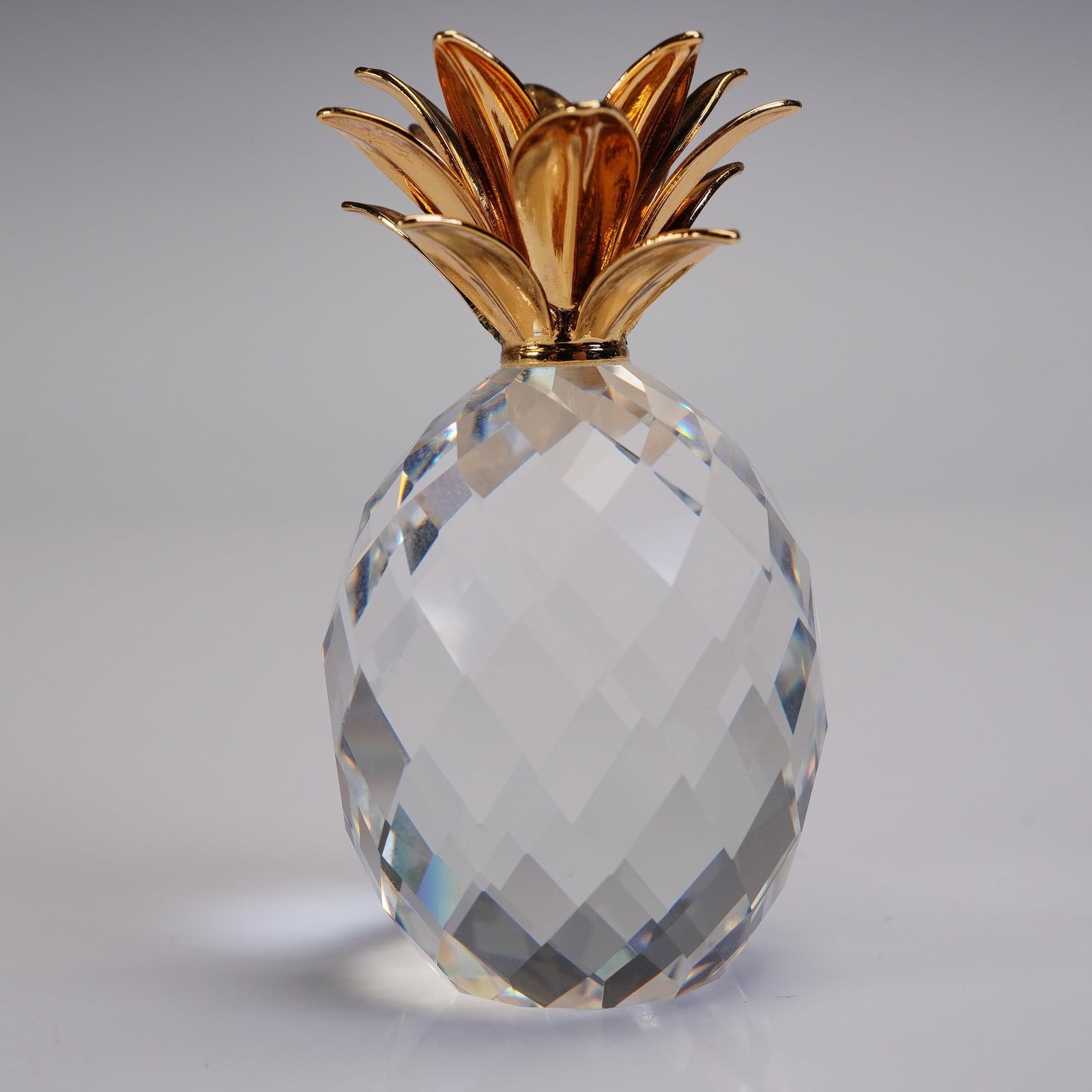 Swarovski Crystal Small Pineapple with Gold Leaves Table Accessory: Faceted clear crystal pineapple figurine by Swarovski, designed by Max Schreck, featuring an intricately detailed gold-tone metal crown of leaves. The body is crafted from precision cut crystal, refle