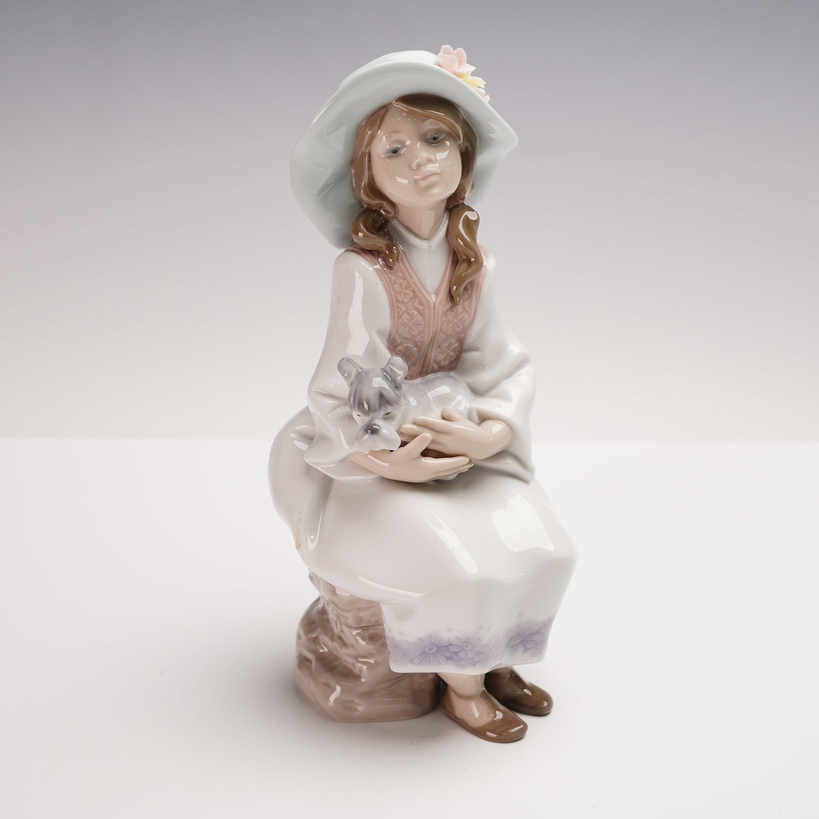Lladro Porcelain Figurine, Daydreams 01006400: Lladro porcelain figurine 01006400, titled Daydreams, sculpted by Francisco Polope. Issued in 1997 and retired in 2004, this serene piece features a young girl in a wide-brimmed hat seated with a smal