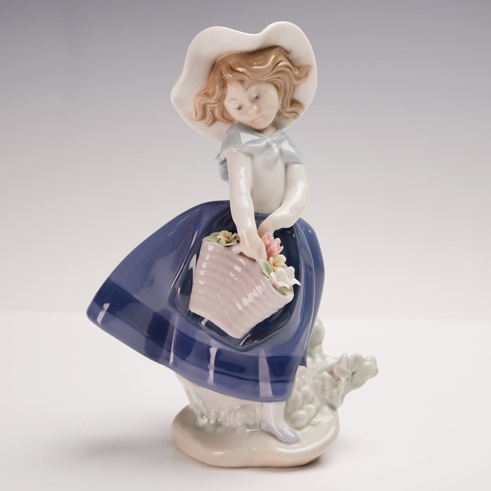 Lladro Porcelain Figurine, Pretty Pickings 1005222: A graceful young girl pauses in the breeze, holding a basket filled with pastel flowers. This Lladro porcelain figurine, titled Pretty Pickings, was sculpted by Jose Puche and issued in 1984. She wear