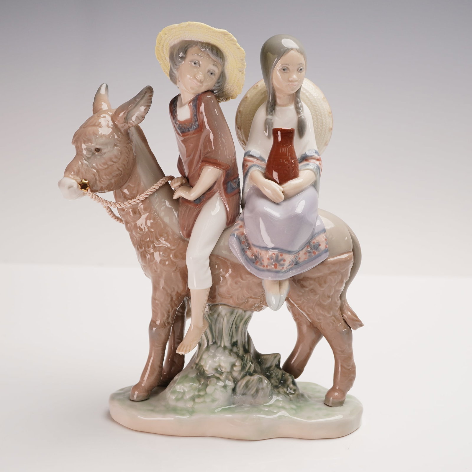 Lladro Porcelain Figurine, Ride in the Country 01005354: Lladro porcelain figurine 01005354, titled Ride in the Country, sculpted by Jose Puche. Issued in 1986 and retired in 1994, this charming piece portrays two children riding together on a donkey, with 
