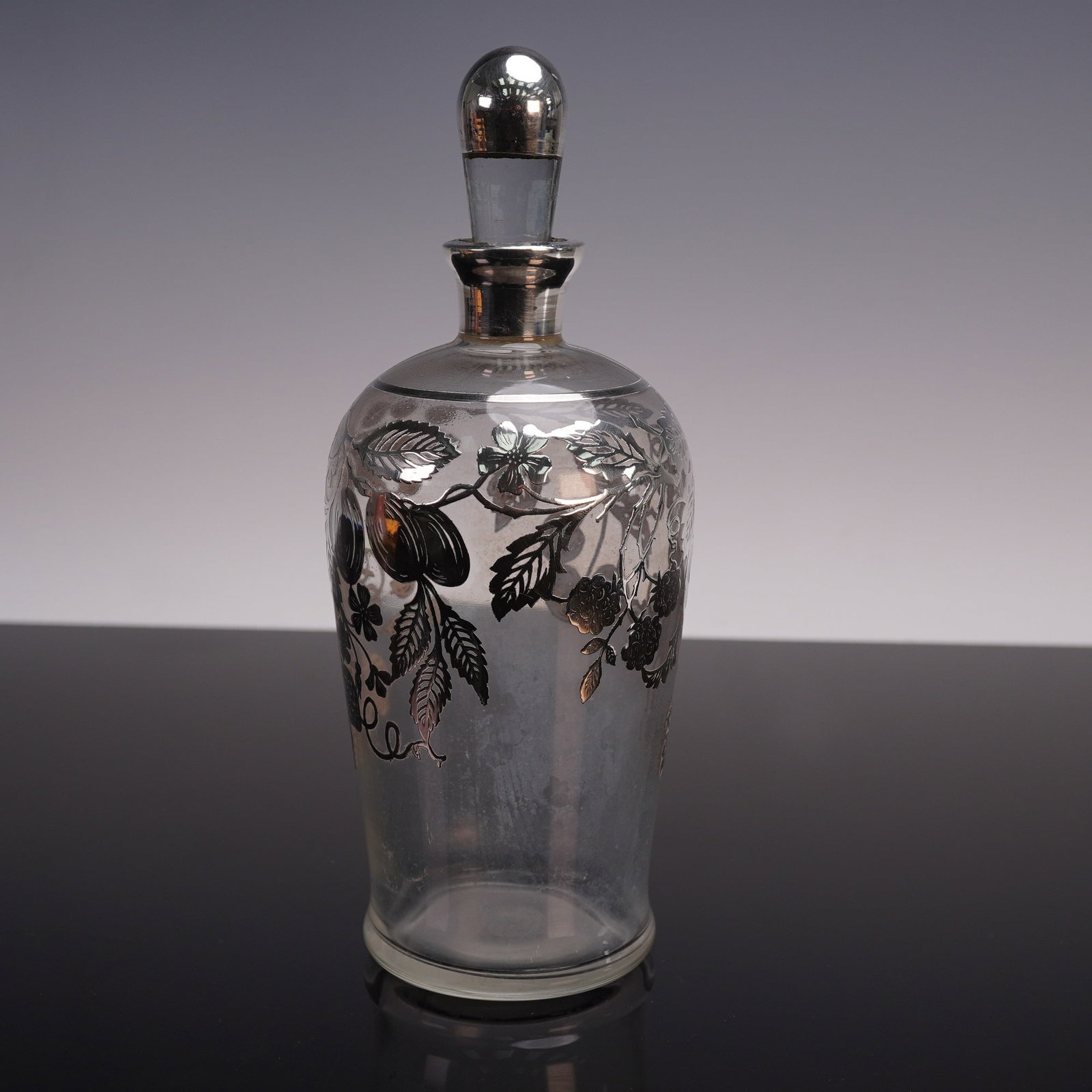 Vintage Glass Decanter with Sterling Silver Floral Overlay: A vintage glass decanter featuring an elegant sterling silver floral overlay. The piece is topped with a silver-coated stopper and showcases a delicate design of leaves and berries etched on the surfa