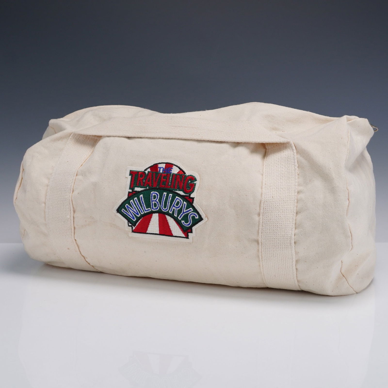 The Traveling Wilburys Promotional Tote Bag: A vintage style canvas tote bag emblazoned with the unmistakable embroidered insignia of The Traveling Wilburys; a supergroup known for its late 1980s musical collaboration. Fashioned from a natural c