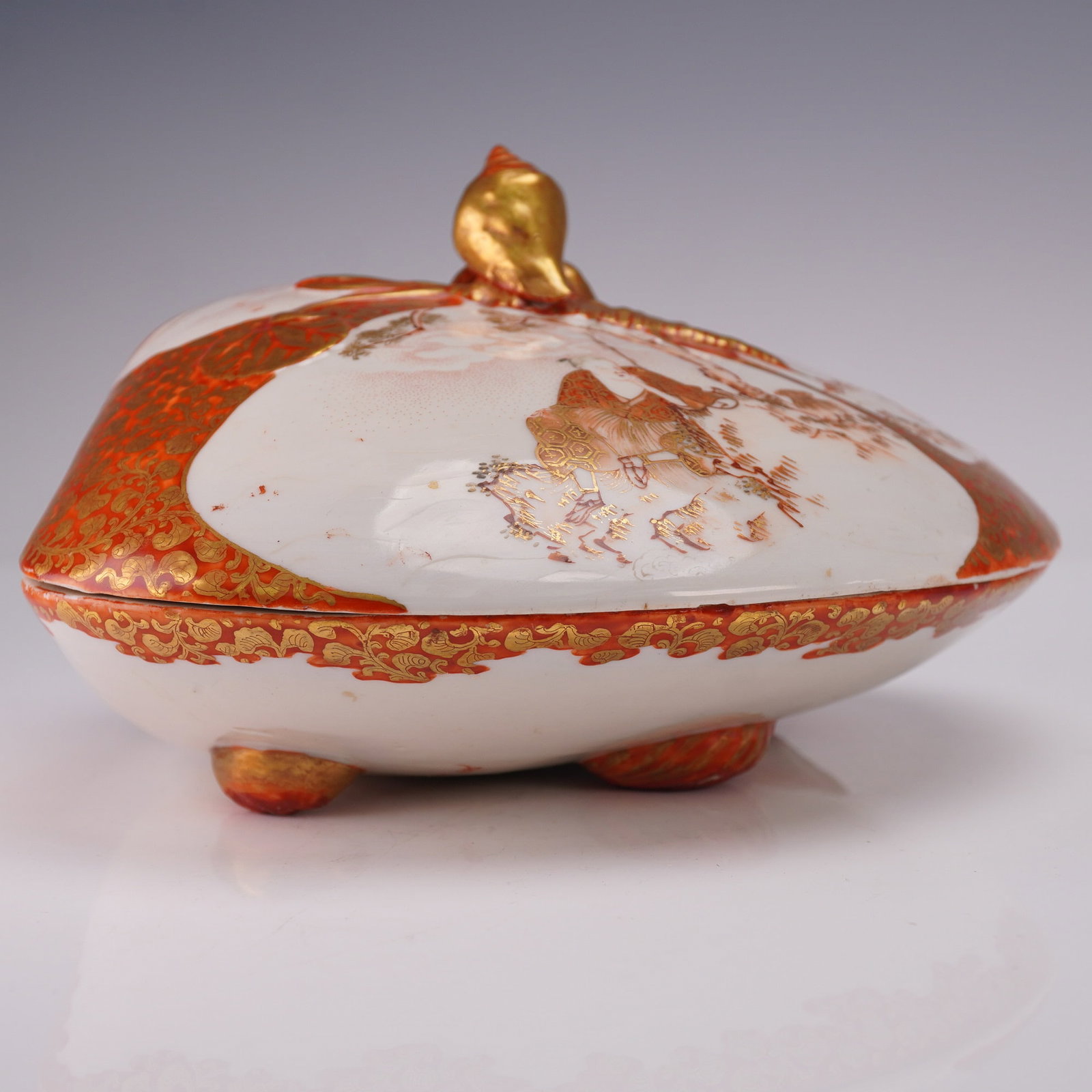 2pc Japanese Kutani Red and Gilt Clam Box with Lid: A porcelain box in the form of a clam shell, comprised of a base and matching lid. The exterior is decorated in iron red and gilt with alternating panels featuring figural scenes, landscapes, and intr