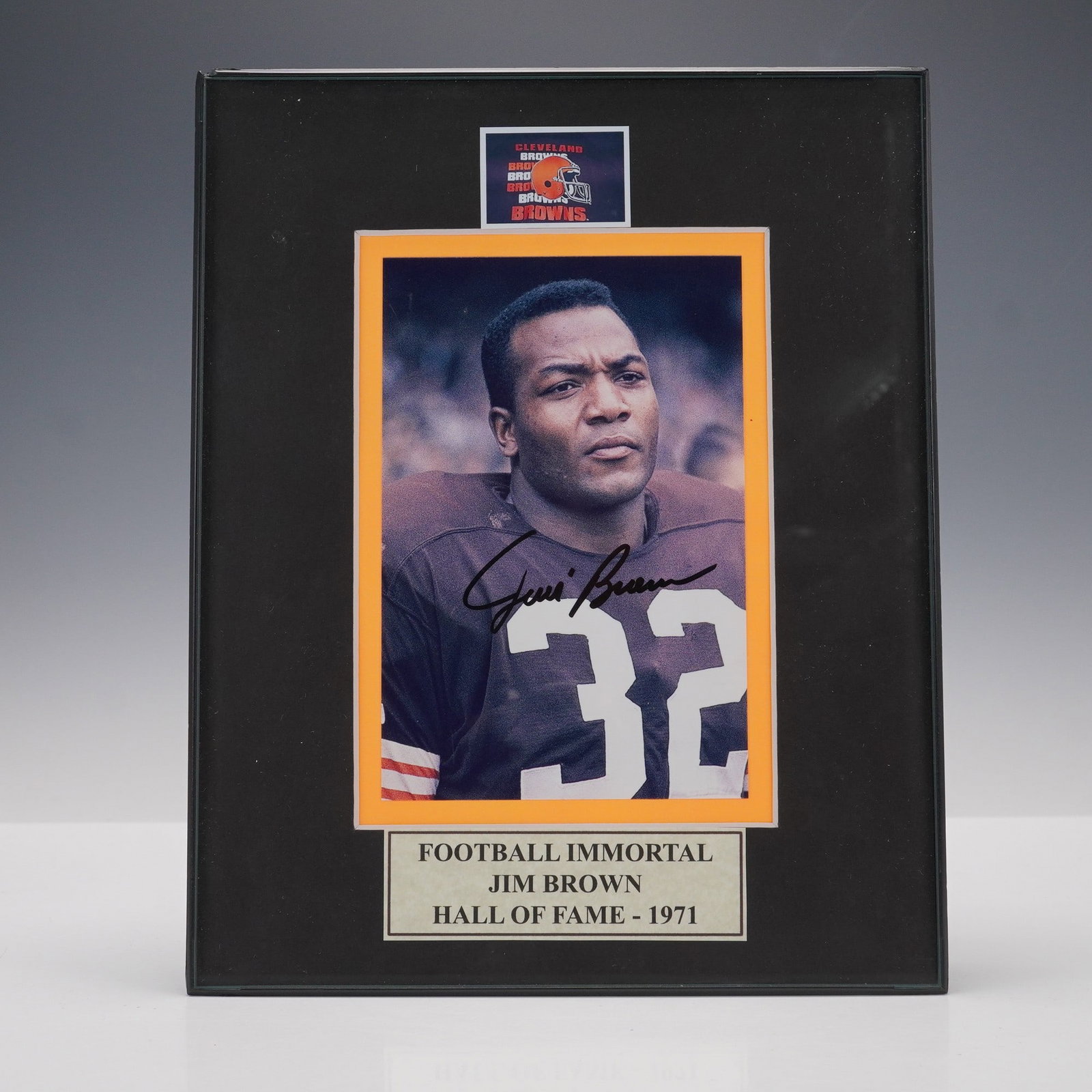 Jim Brown Autographed Hall of Fame Photograph: Framed color photograph of legendary Cleveland Browns running back Jim Brown, signed in bold black marker across his jersey. The image features Brown in his No. 32 uniform, with a mounted plaque readi