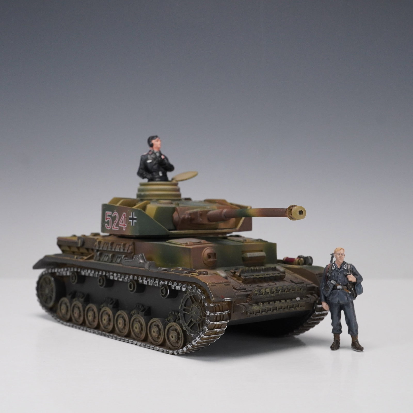 2pc Britains Panzer IV Model Tank and German Soldier Figures: A 2-piece grouping featuring a highly detailed Britains Panzerkampfwagen IV tank model and two Wehrmacht soldier figures. The Panzer IV is finished in a realistic WWII-era camouflage scheme and bears 