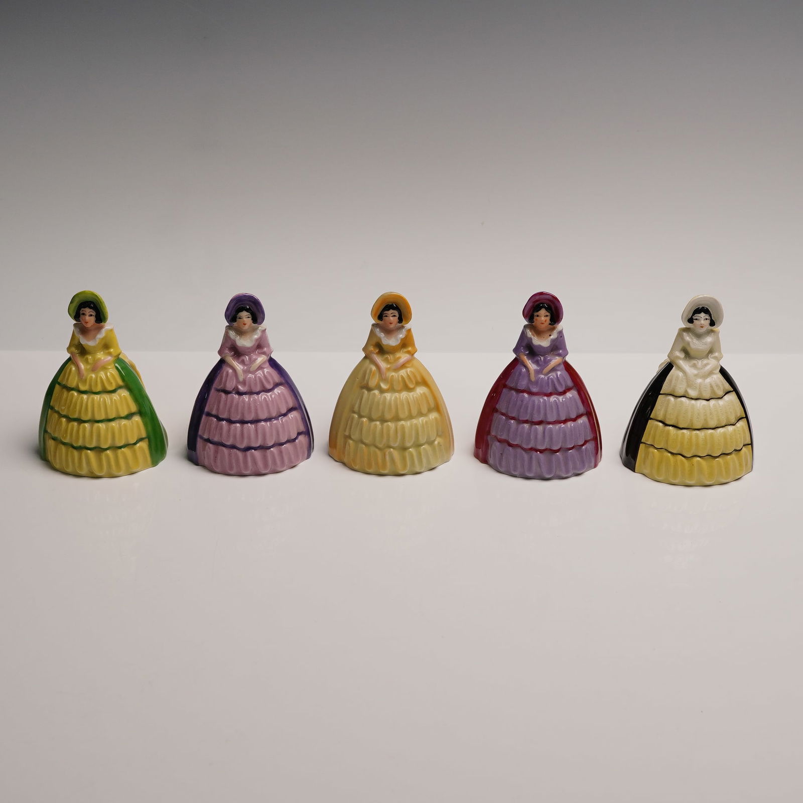 5pc Carlton Ware Figural Napkin Rings: Charming set of five figural napkin rings by Carlton Ware, each molded in the form of a Victorian-style lady wearing a full crinoline dress. The figures are hand-painted in a vibrant and varied palett