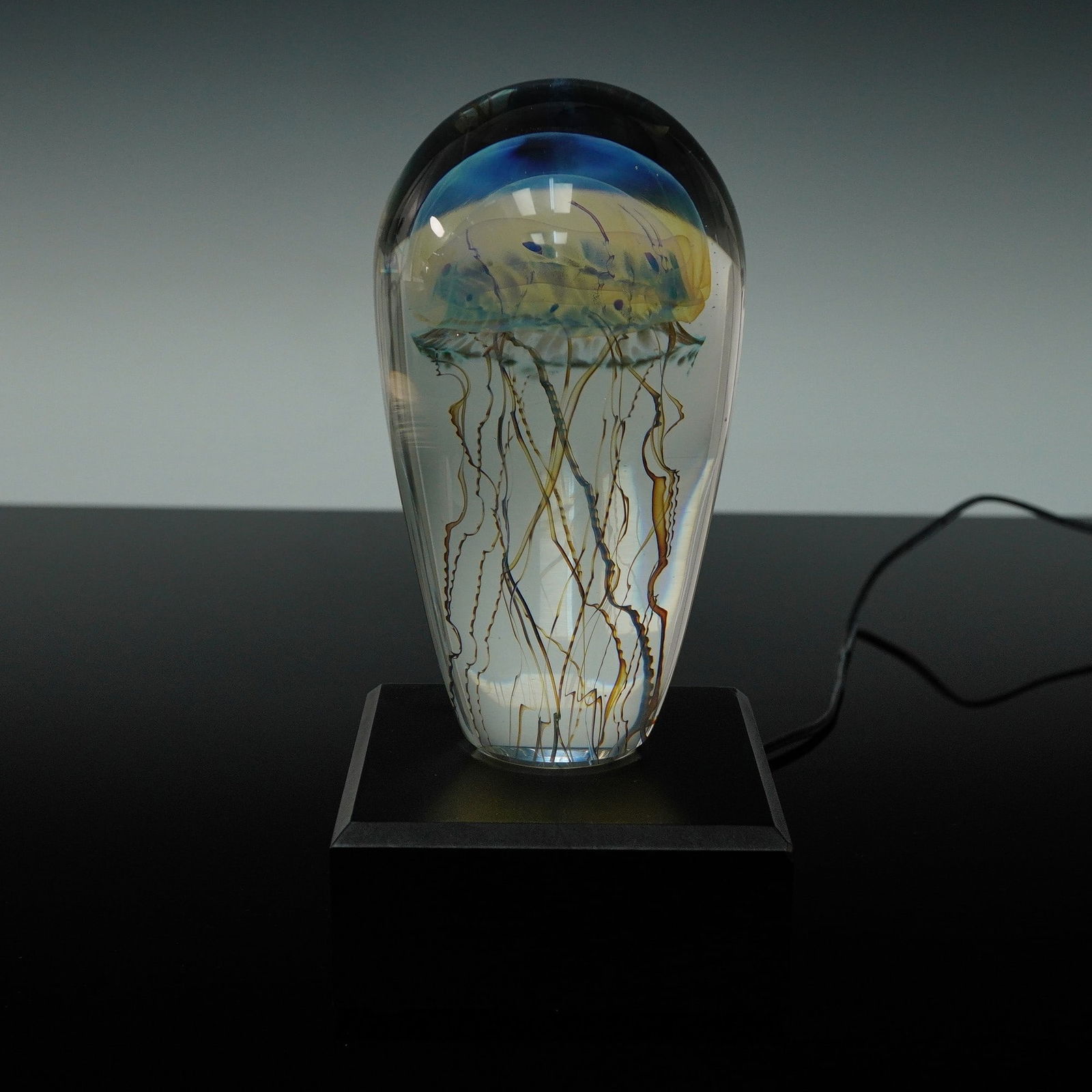 Richard Satava Art Glass Jellyfish Sculpture with Lighted Base: A mesmerizing studio art glass sculpture by Richard Satava, showcasing his iconic jellyfish design encased in clear glass. This handcrafted piece features a brilliantly colored jellyfish with a domed,
