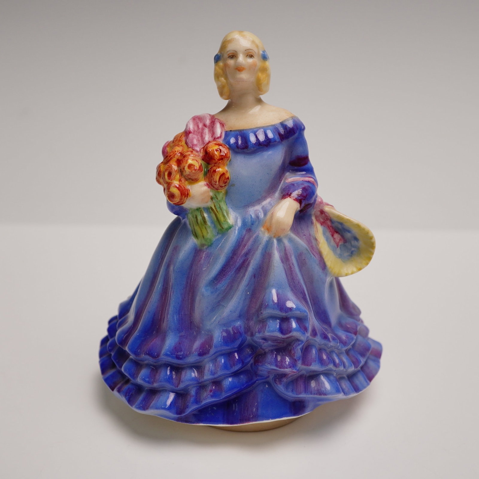 Royal Worcester Figurine, June by S.V. Williams and J.S. Bray: A delightful Royal Worcester bone china figurine titled June, hand-painted in vivid tones of blue, violet, and coral. The figure portrays a young woman in a flounced gown holding a vibrant bouquet of 