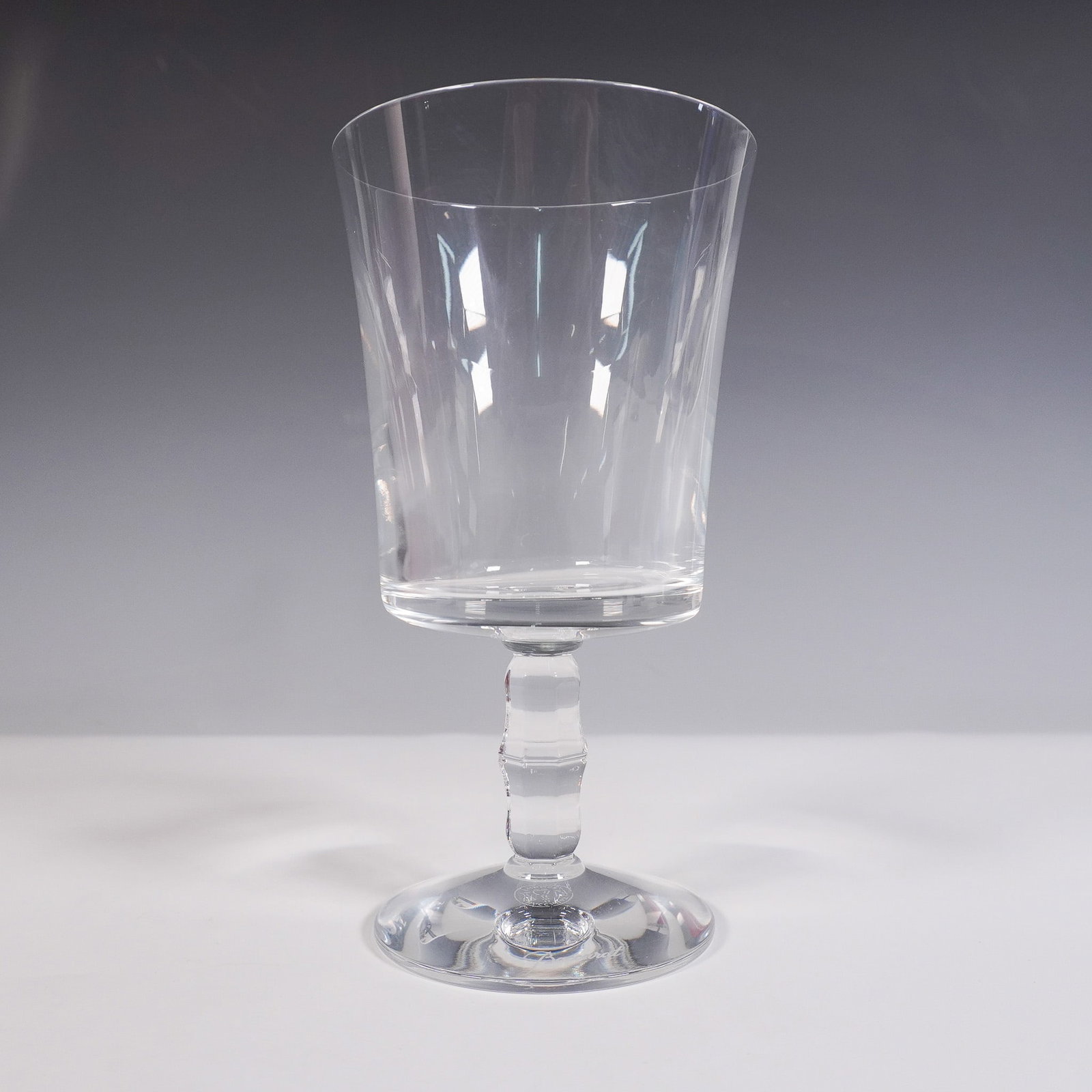 Baccarat Crystal Wine Glass, Embassy: A clear crystal wine glass featuring a plain, squarish bowl and a faceted wafer stem. The base is etched with the Baccarat logo and factory hallmark. This item is presented in its original red Baccara