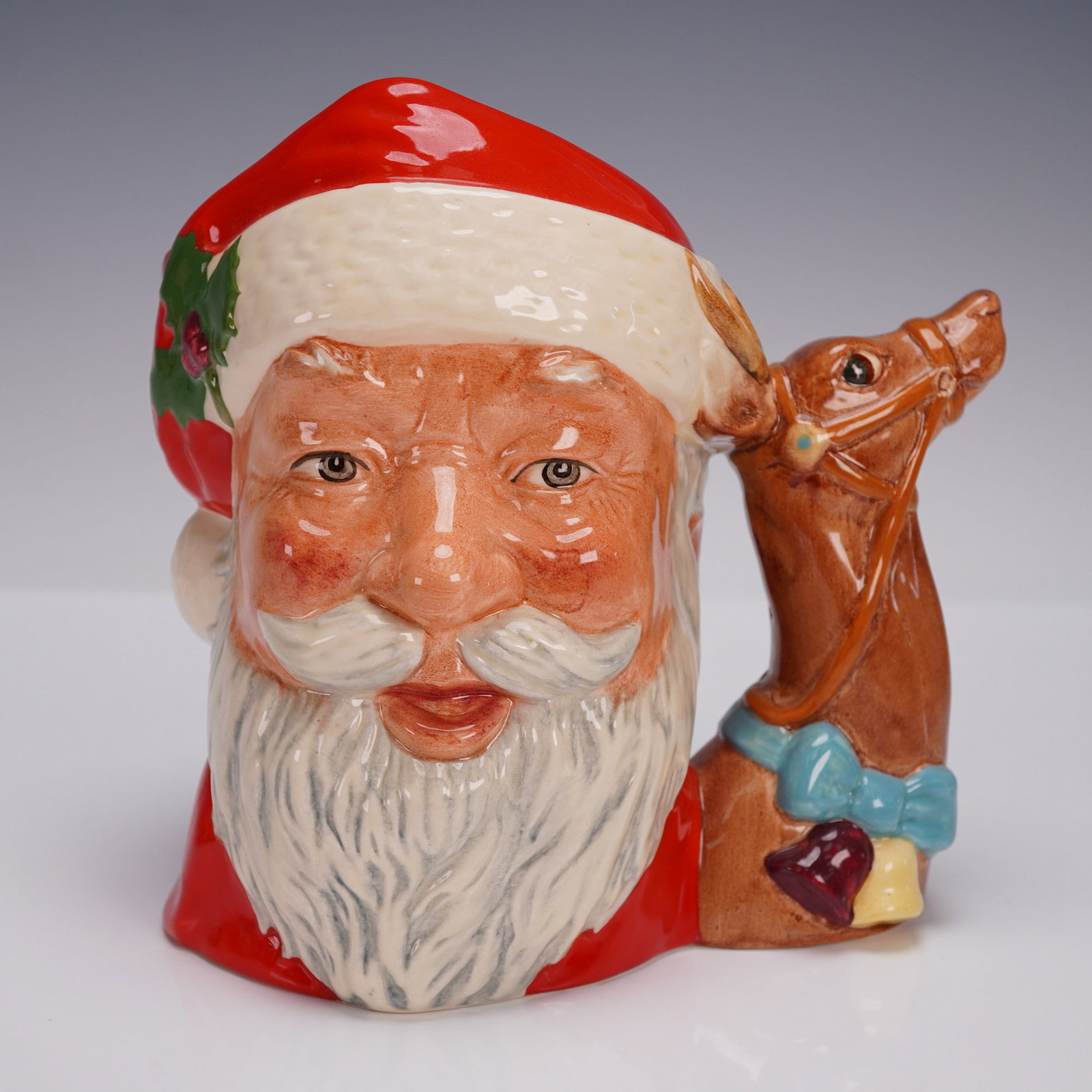 Royal Doulton Character Jug, Santa Claus D6675: Large Royal Doulton character jug, Santa Claus D6675, modeled with a cheerful bearded face wearing a red hat adorned with holly, accompanied by a brown reindeer handle decorated with a blue bow and Ch