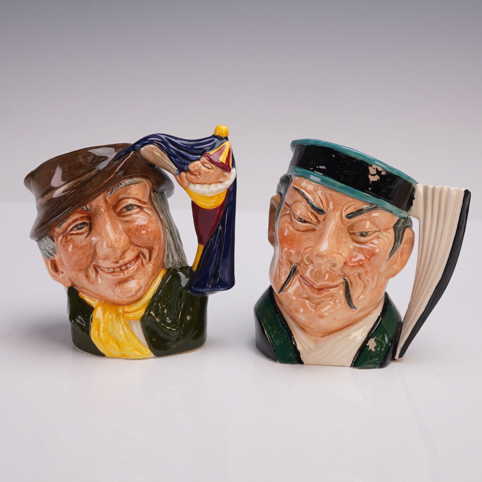 2pc Royal Doulton SM Character Jugs- Punch & Judy D6593 & The Mikado D6593: Pair of Royal Doulton small character jugs, each hand-painted with fine detail and marked with Royal Doulton backstamps to the undersides. Includes Punch & Judy Man (D6593, designer: David B. Biggs, C
