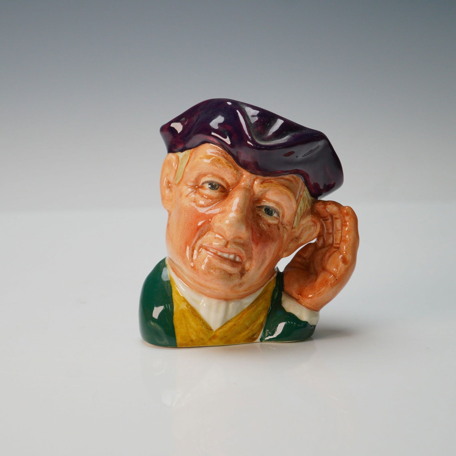 Royal Doulton Small Character Jug, Ard of Earing D6591: Dark purple tricorn; green, white, and yellow clothing. With handheld to cup his ear, this cockney gentleman is a comic representation of a deaf man. Royal Doulton backstamp. Artist: David B. Biggs Is