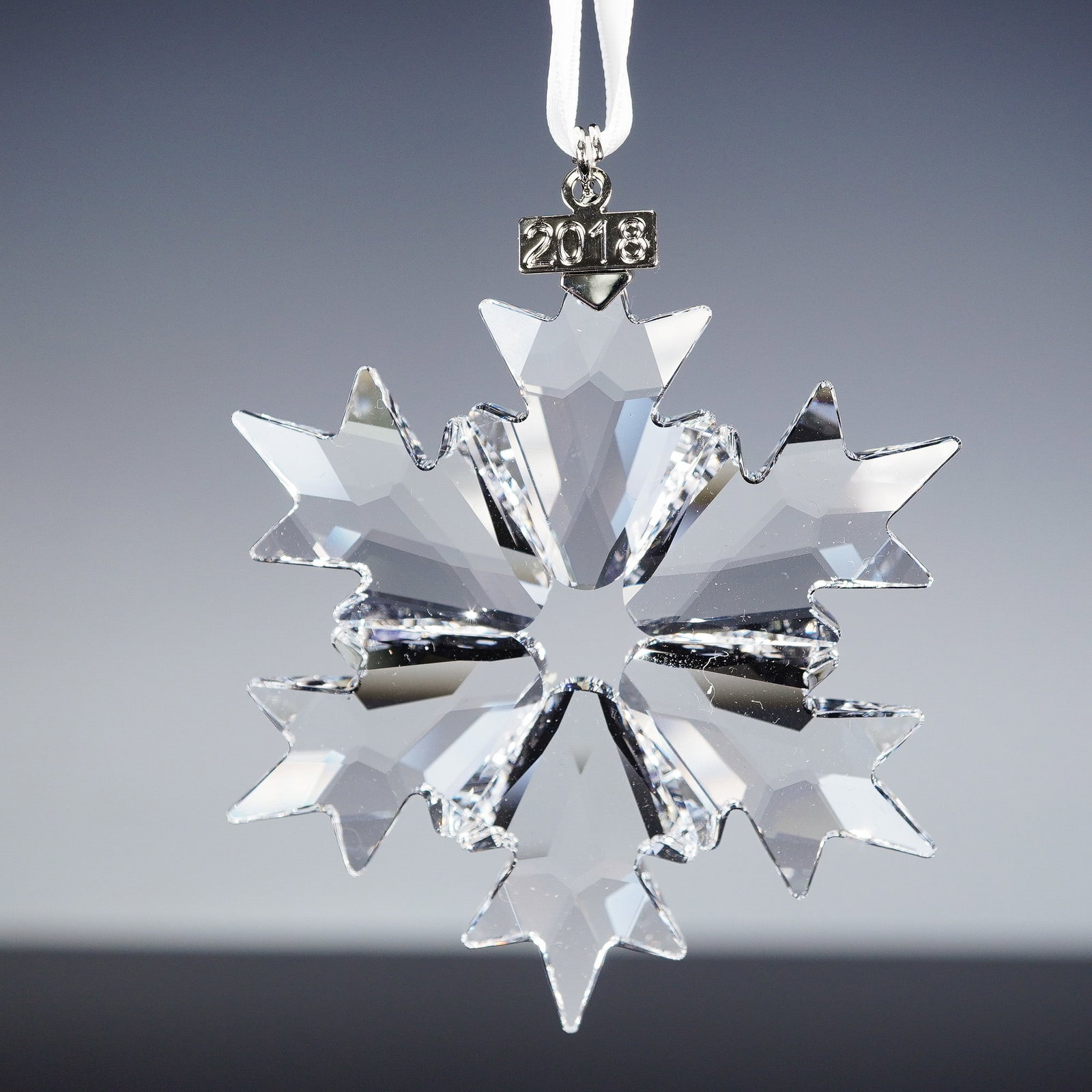 Swarovski Crystal 2018 Christmas Ornament: The 2018 annual edition ornament features a striking snowflake design cut with 156 sparkling clear crystal facets. Designed by Verena Castelein, it hangs from a white satin ribbon and includes a polis