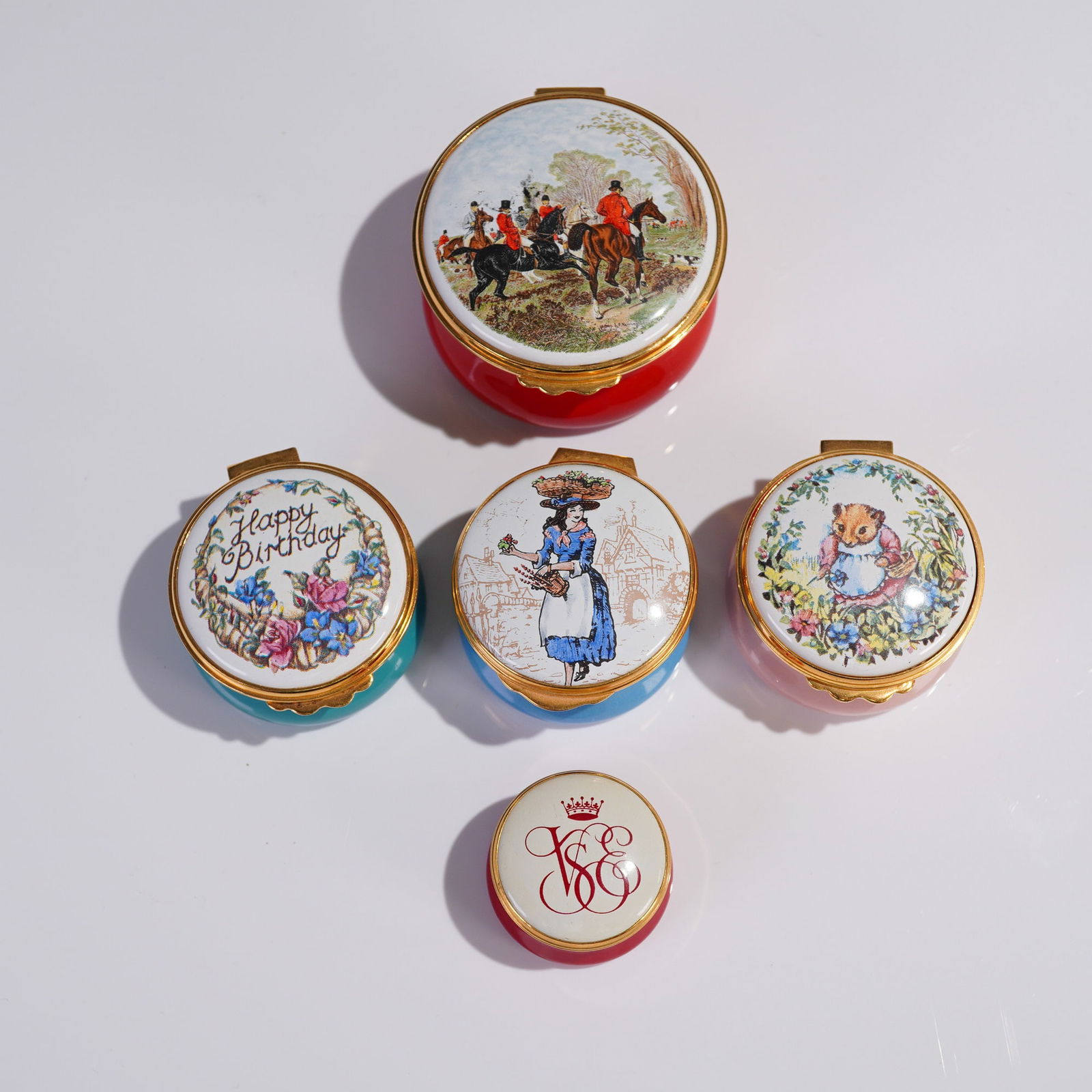 5pc Kingsley Enamels & Others, English Enamel Pill Boxes: A charming assortment of five English enamel pill and trinket boxes. Included are four larger hinged enamel boxes and one miniature. The collection features a red enamel box with a fox hunting scene o