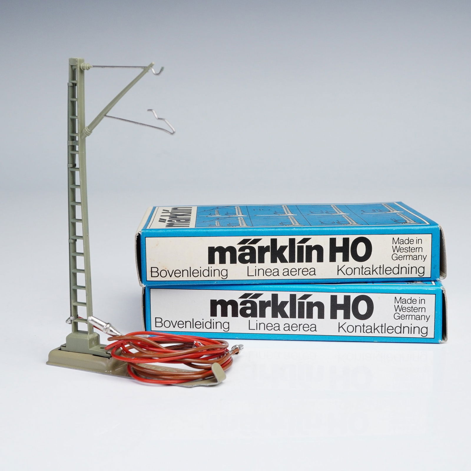 2pc Marklin Catenary System Parts, HO 7010: Pair of Marklin HO 7010 M catenary system components, each housed in its original blue and white box. The set includes upright mast poles with insulators and wire arms, designed for overhead line oper