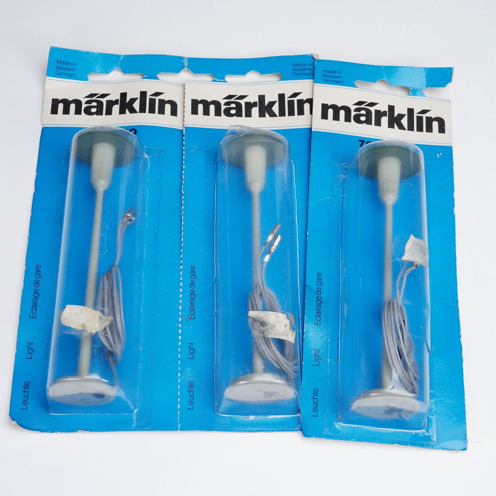 3pc Marklin Model Street Lamp Set, Light 7047HO: Set of three Marklin model street lamps. Each lamp is packaged in original blue blister packaging labeled with product details in multiple languages including Leuchte, Light, and Eclairage de gare. Th