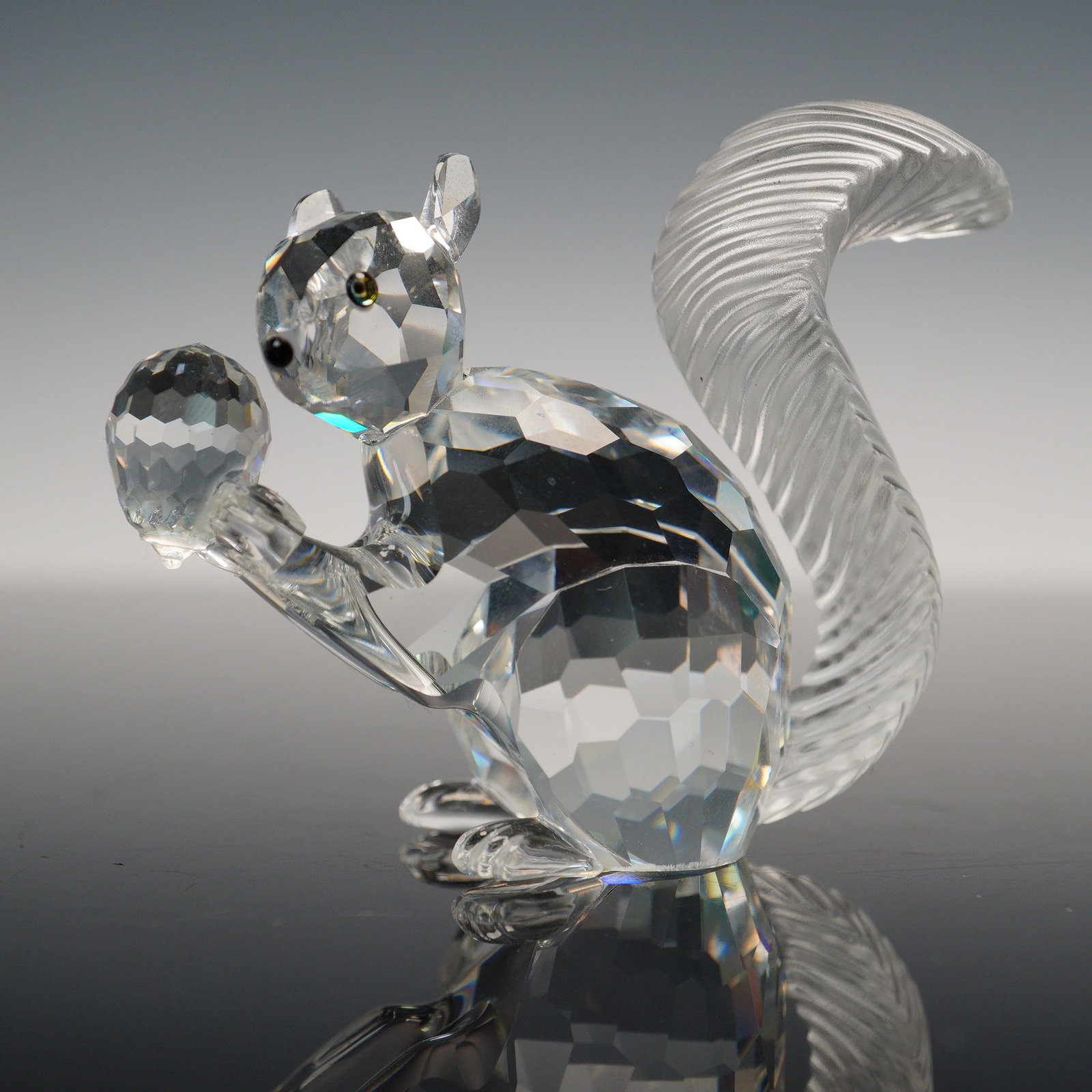Swarovski Crystal Figurine, 1997 Squirrel 208433: A finely crafted Swarovski crystal figurine of a squirrel, featuring a clear faceted crystal body that sparkles with light from every angle. The squirrel is depicted upright holding a faceted crystal 