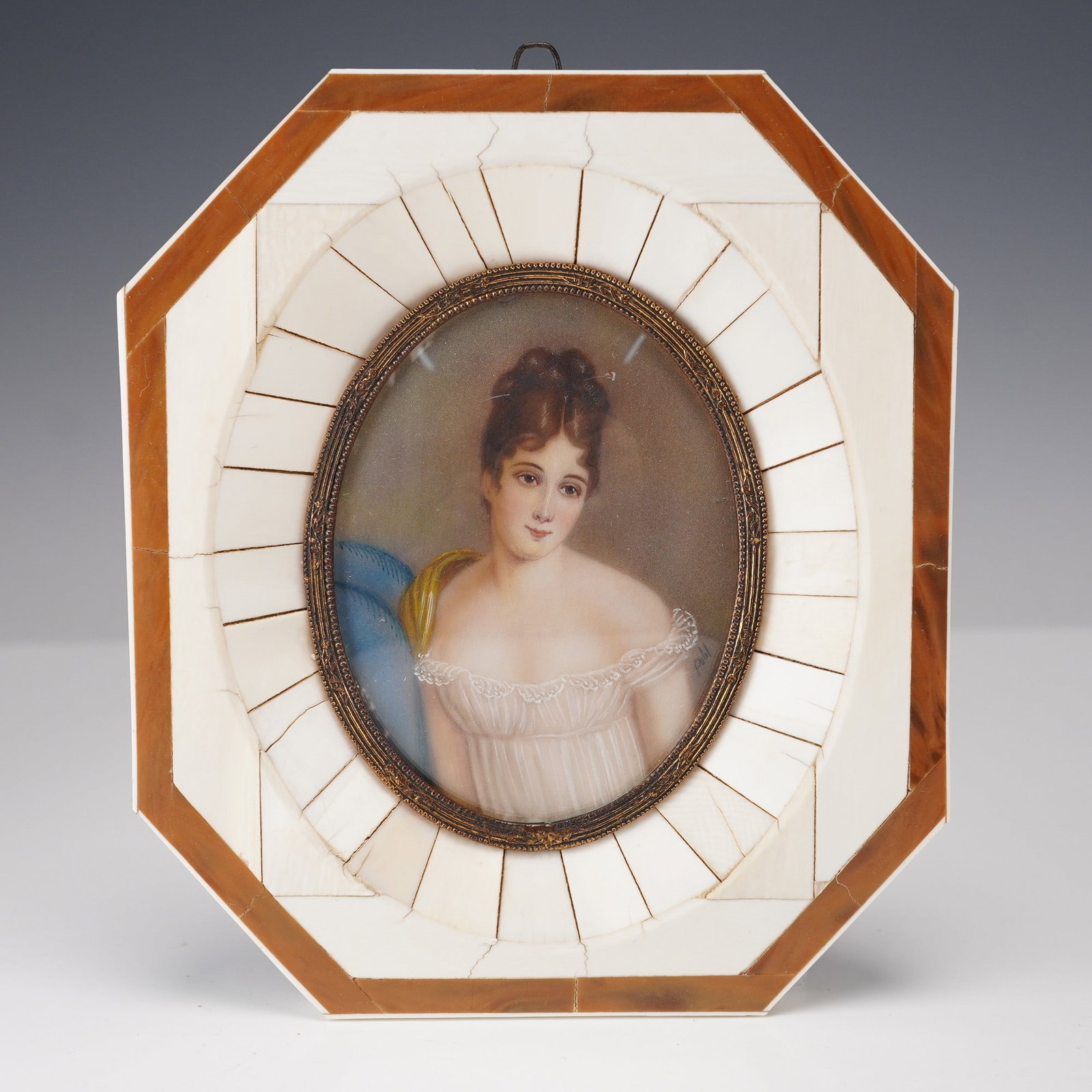 Antique German Hand Painted Portrait Miniature in Octagonal Frame: Antique German portrait miniature featuring a finely hand-painted depiction of a young woman in a white empire waist gown with lace trim and a blue wrap over her shoulder. The portrait is set under gl