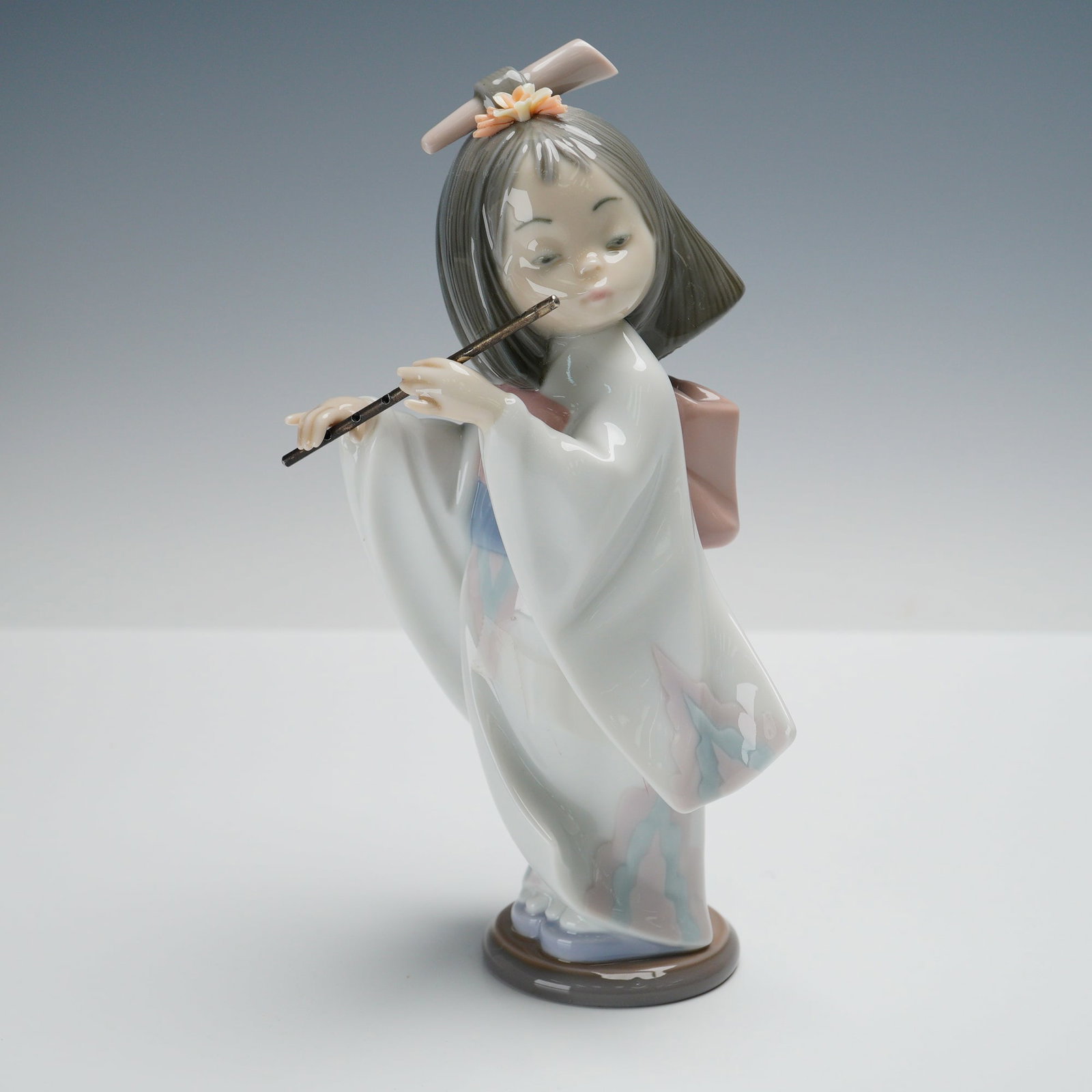 Lladro Porcelain Figurine Playing the Flute 01006150: Lladro porcelain figurine Playing the Flute item number 01006150 sculpted by Salvador Debon in 1994 and retired in 1999 depicting a young girl in a traditional kimono playing a flute with pastel glaze