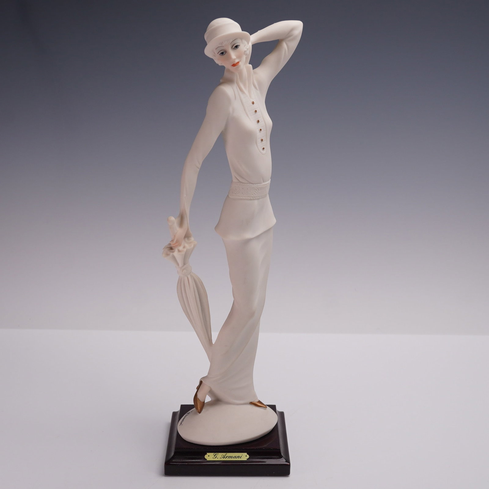 Florence Giuseppe Armani Figurine, Lady with Umbrella: Elegant porcelain figurine depicting a graceful woman in a stylized Art Deco silhouette, holding a parasol in one hand while tilting her head with poised restraint. Mounted on a square wooden plinth w