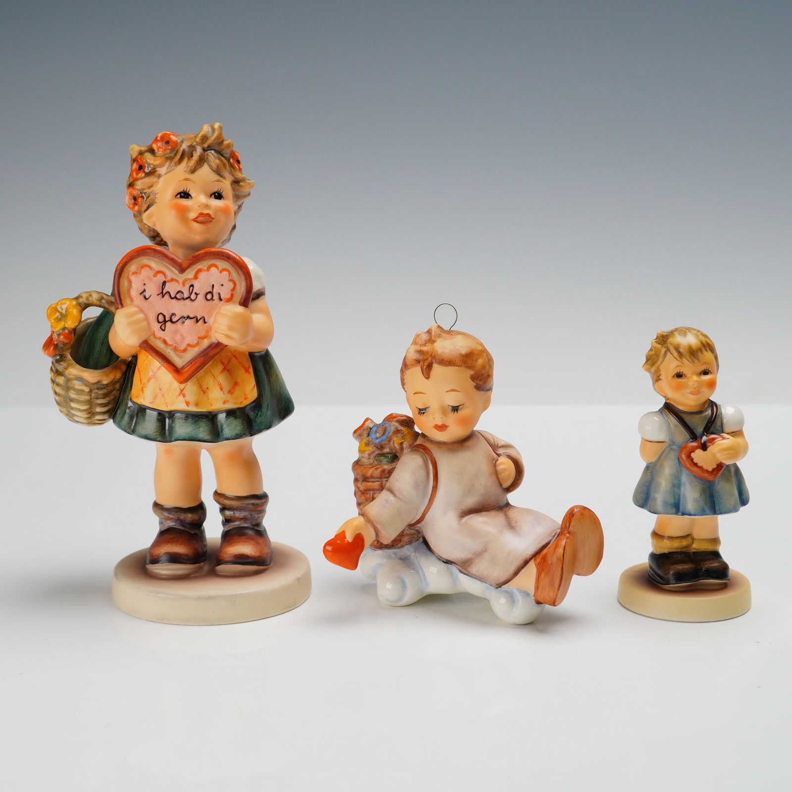 3pc Goebel Hummel Figurines, Expressions of Love: Charming group of three Goebel Hummel porcelain figurines themed around love and affection, including My Heart's Desire (2102/A), depicting a young girl holding a Valentine heart, Love from Above (198