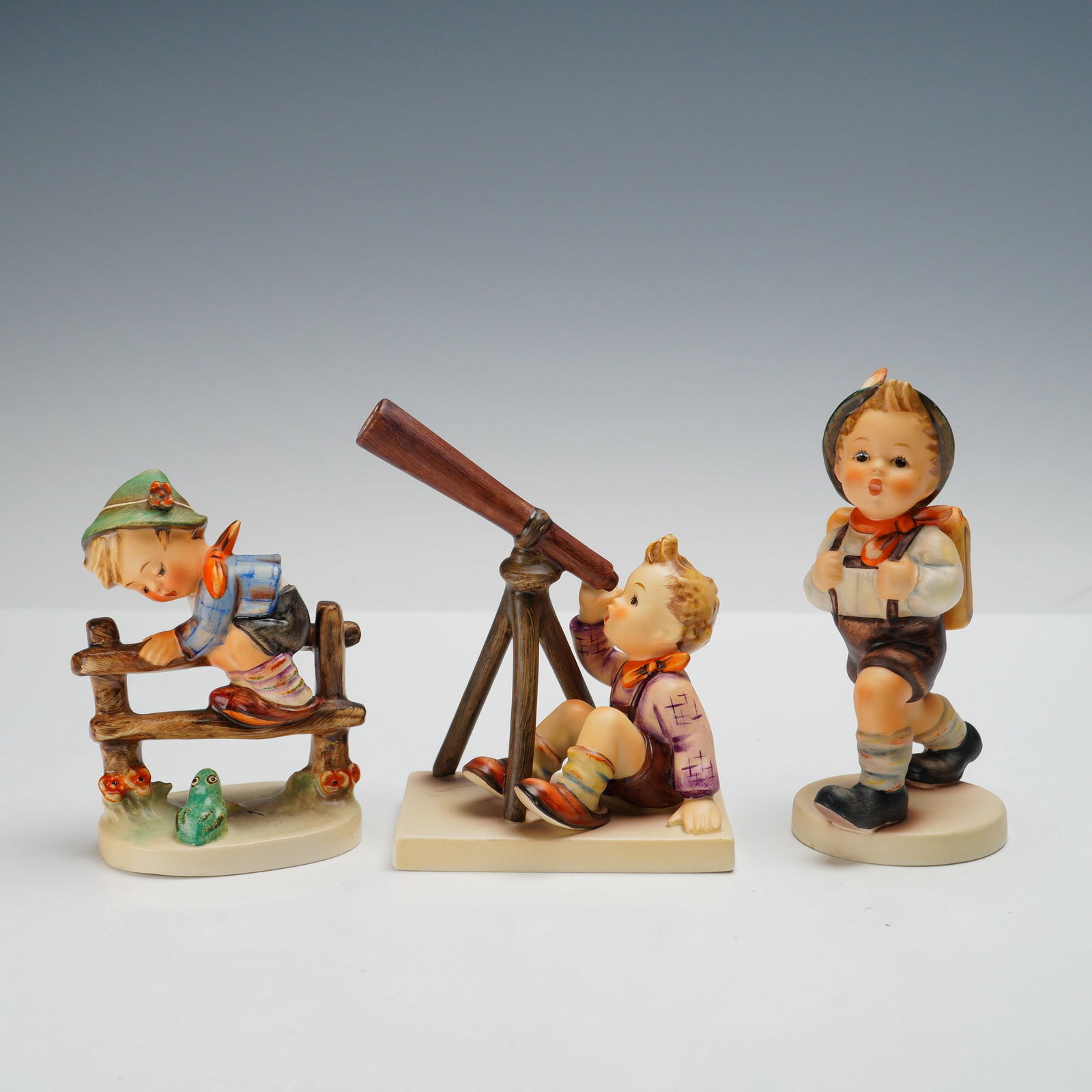 3pc Goebel Hummel Figurines, School Days Grouping: Charming set of three Goebel Hummel porcelain figurines depicting classic childhood scenes. Includes School Boy (82/0), a young boy with knapsack; Retreat to Safety (201/2), a boy climbing a fence sta