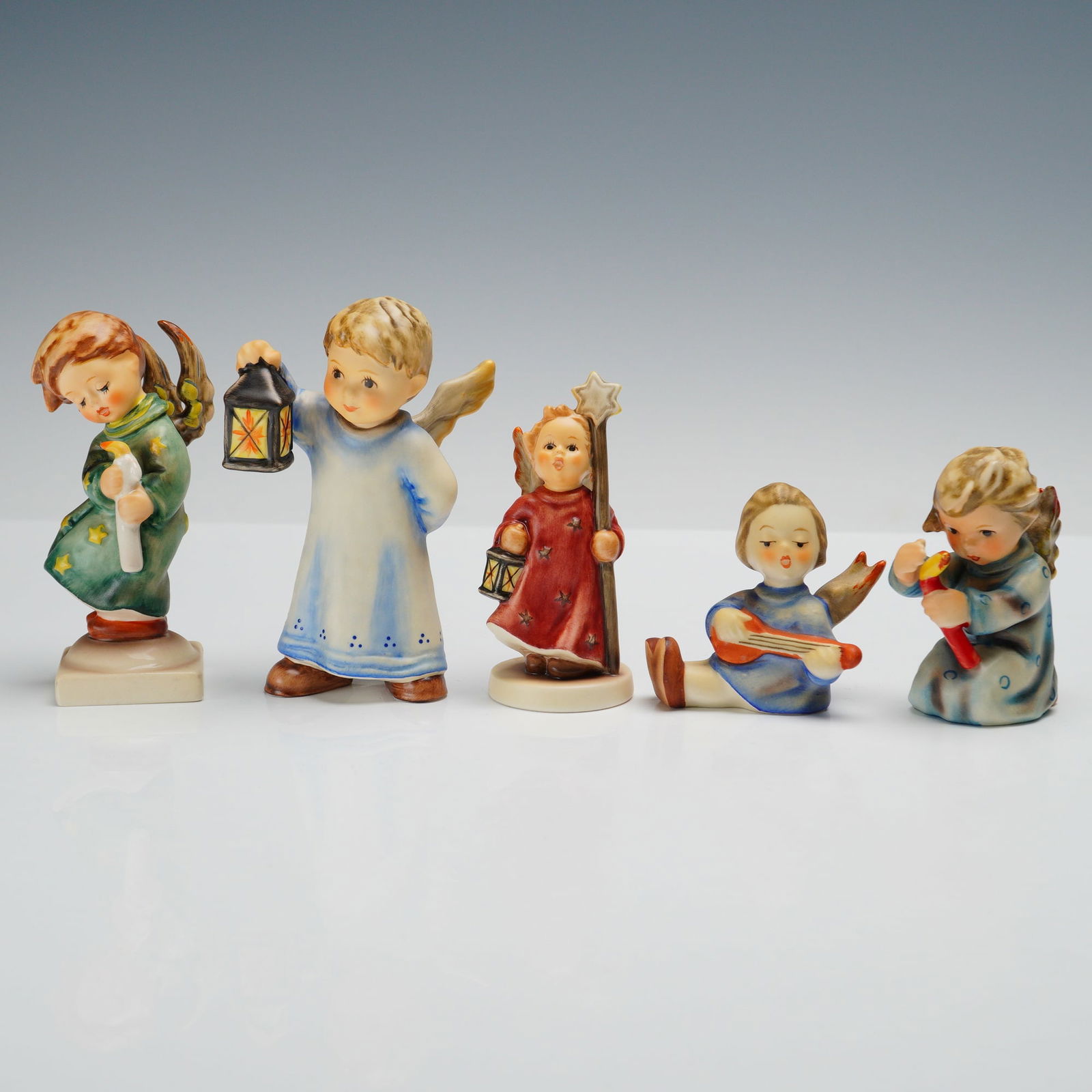 5pc Goebel Hummel Angelic Themed Figurines: This charming collection of five Hummel figurines features angelic designs full of holiday spirit. Heavenly Angel wears a green robe and gently holds a scroll. Joyous News is dressed in blue and plays