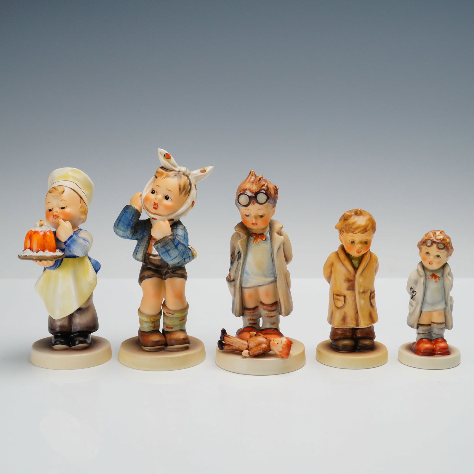 5pc Goebel Hummel Figurines: Set of 5 Goebel Hummel figurines including Too Shy to Sing, Doctor, The Doctor, Baker, and Toothache. Too Shy to Sing is a boy in a long coat with his arms folded, looking bashful. Doctor is the small