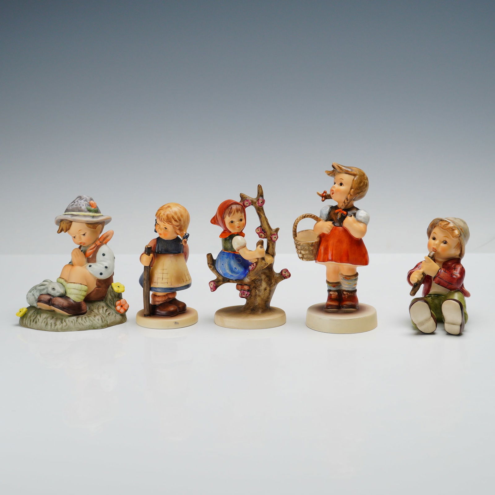 5pc Goebel Hummel Figurines: A charming set of five Goebel Hummel figurines. Pixie depicts a blonde girl in a dress and apron holding a walking stick, a sweet countryside pose. Shepherd with Flute shows a young boy seated and pla