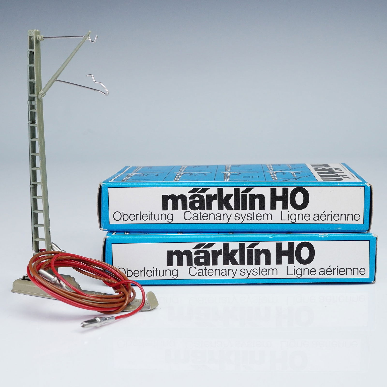 2pc Marklin Catenary System Parts, HO 7010: Marklin HO 7010 M catenary system masts with original boxes. Each unit is made in Western Germany and constructed of a metal base with vertical support, fitted with overhead wire arms and insulators.
