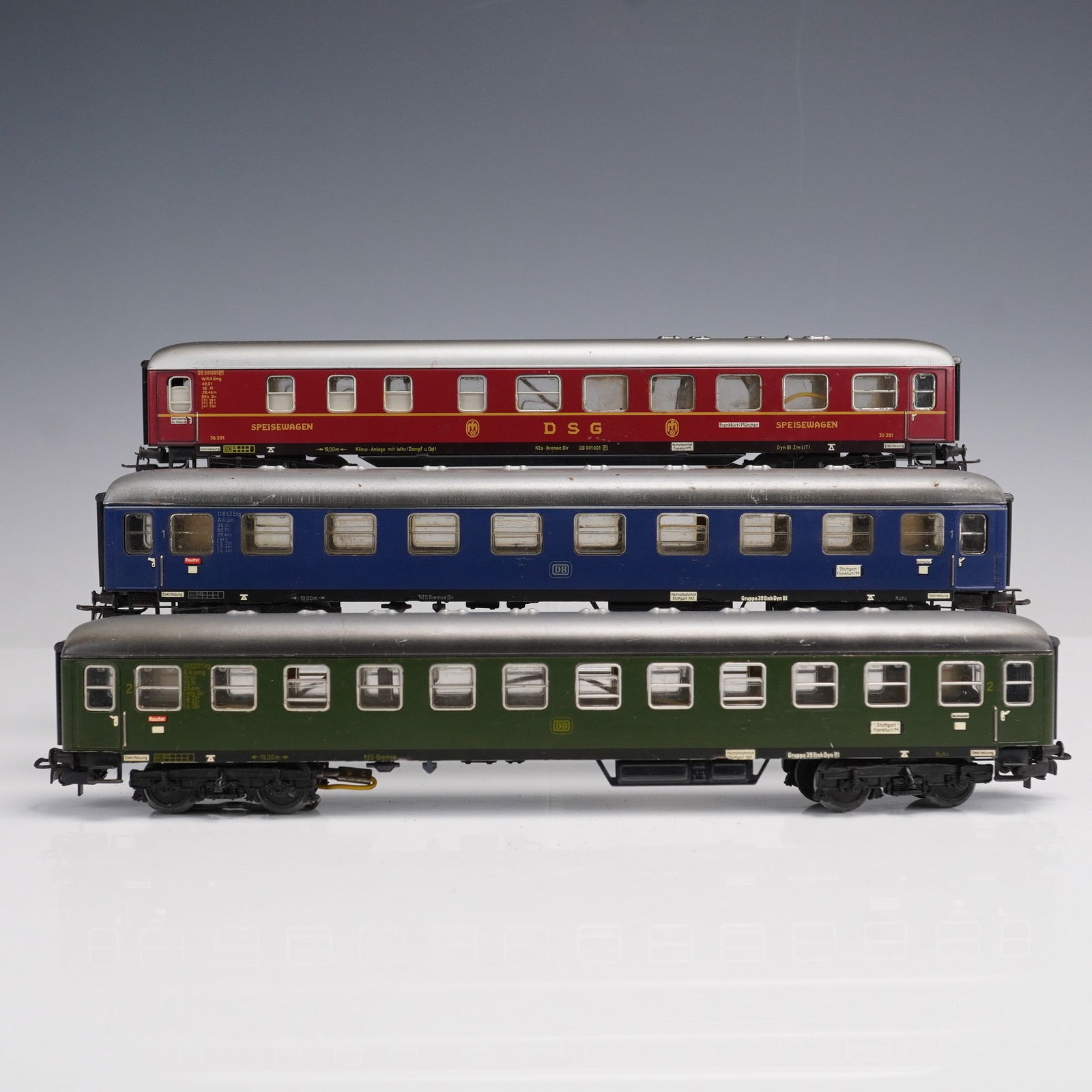 3pc Marklin HO Gauge German Passenger Coaches: A set of three vintage Marklin HO gauge passenger coaches, made in Western Germany, including a red and silver DSG dining car, a blue Deutsche Bundesbahn sleeper coach, and a green Deutsche Bundesbahn