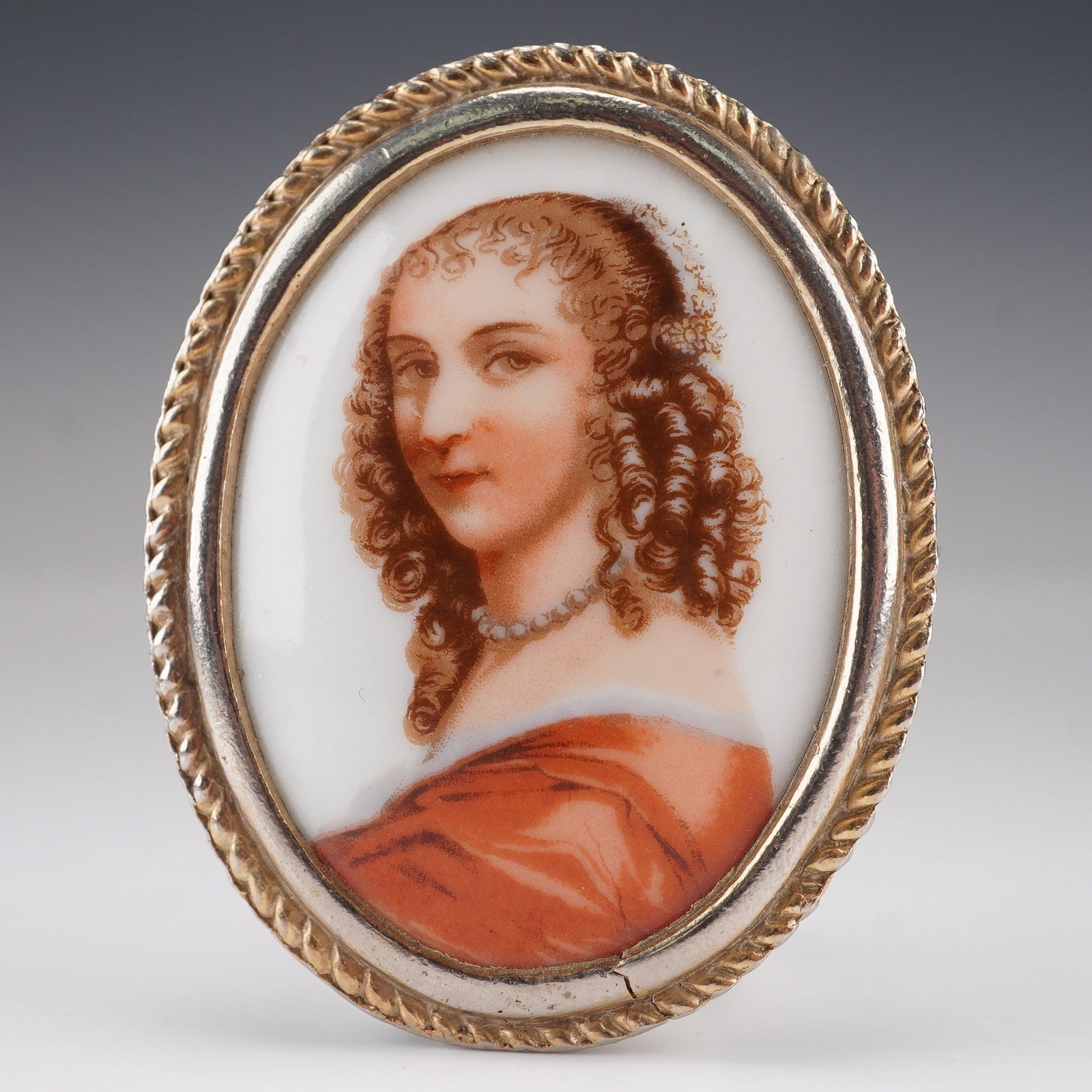 Limoges Porcelain Portrait Brooch or Pendant Oval Frame: Oval portrait brooch or pendant featuring a finely decorated Limoges porcelain disk depicting a woman in a red gown with curled hair and pearl necklace. The porcelain is set in a delicate rope-twist e