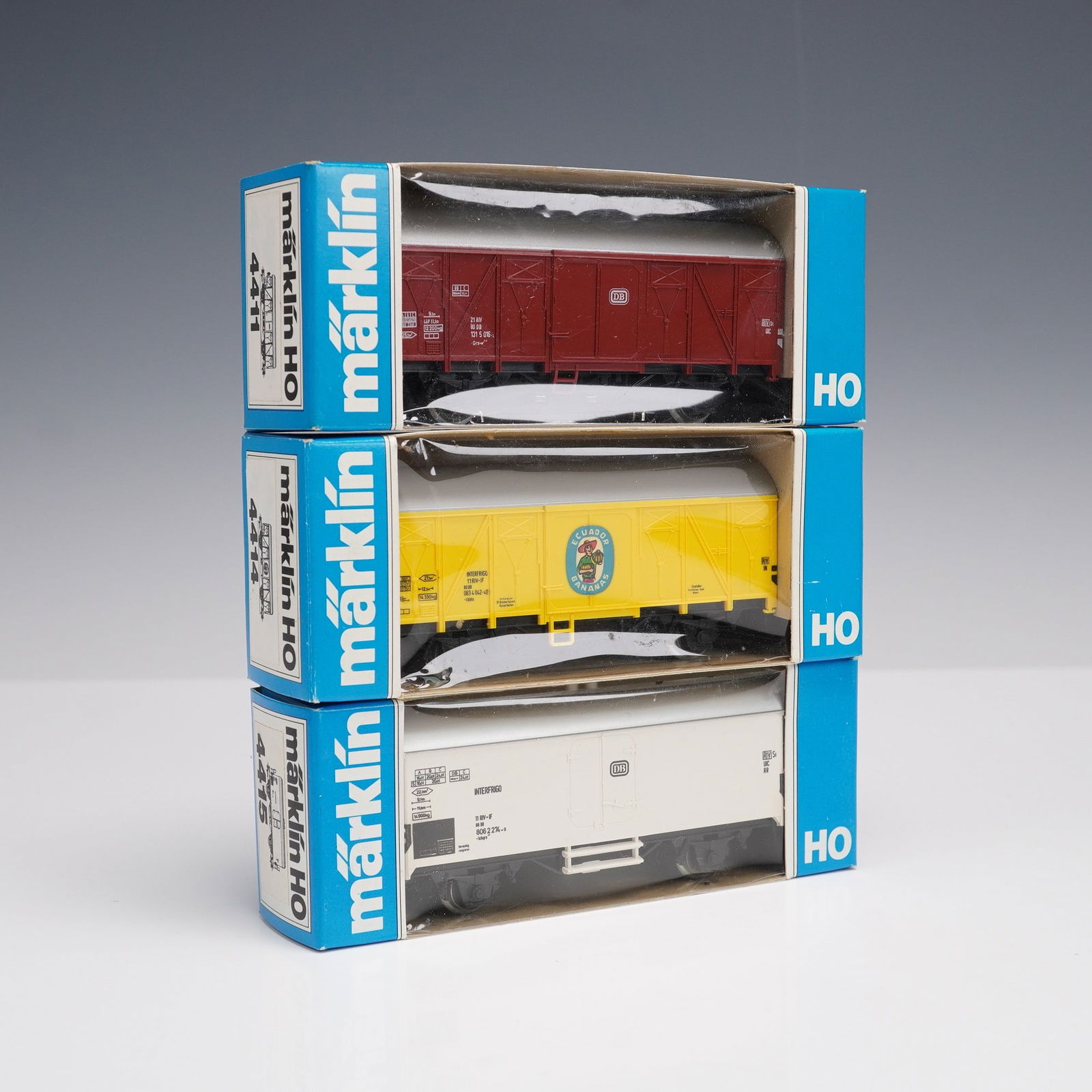 3pc Marklin HO Scale Freight Cars: Group of three Marklin HO scale model freight cars, made in Western Germany, each housed in original blue window boxes. Includes a maroon Deutsche Bundesbahnen boxcar with silver roof, a yellow Ecuado