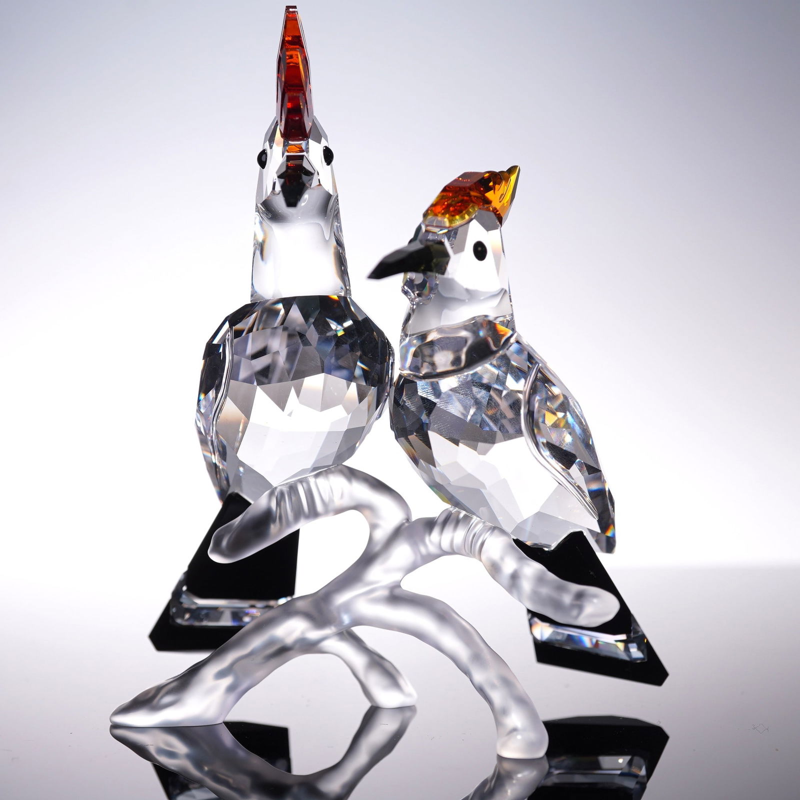 Swarovski Crystal Figurine, Hoopoes: Part of the Feathered Beauties collection. A pair of birds perched on a frosted branch. The birds are clear crystal with black diamond crystal beaks. The feathery crown are medium topaz crystal, and c
