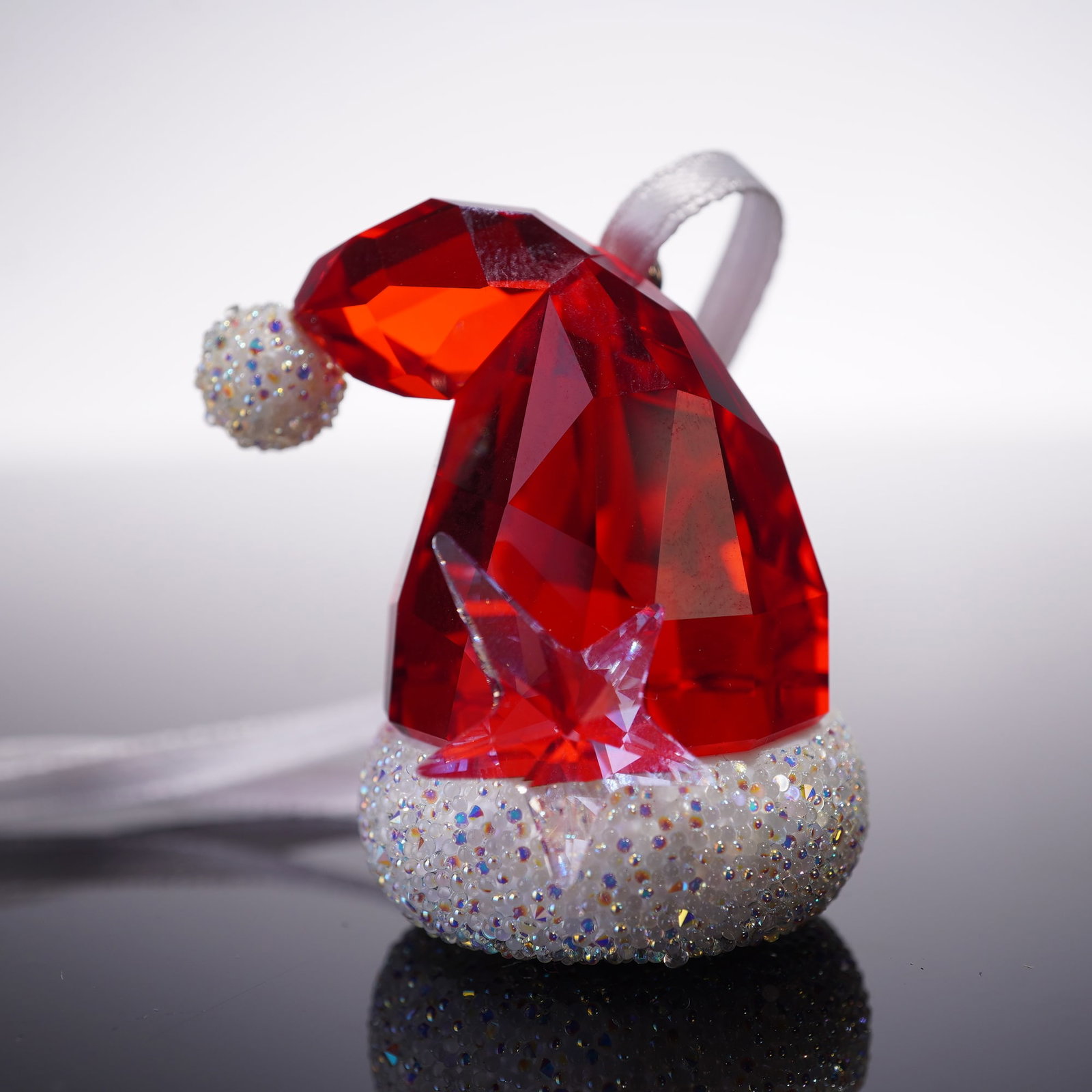 Swarovski Crystal Christmas Ornament, Santa's Hat: The ornament is crafted in faceted red crystal with a clear crystal star accent and a glittering white crystal base and pom-pom. It is fitted with a hanging ribbon and features the Swarovski swan impr