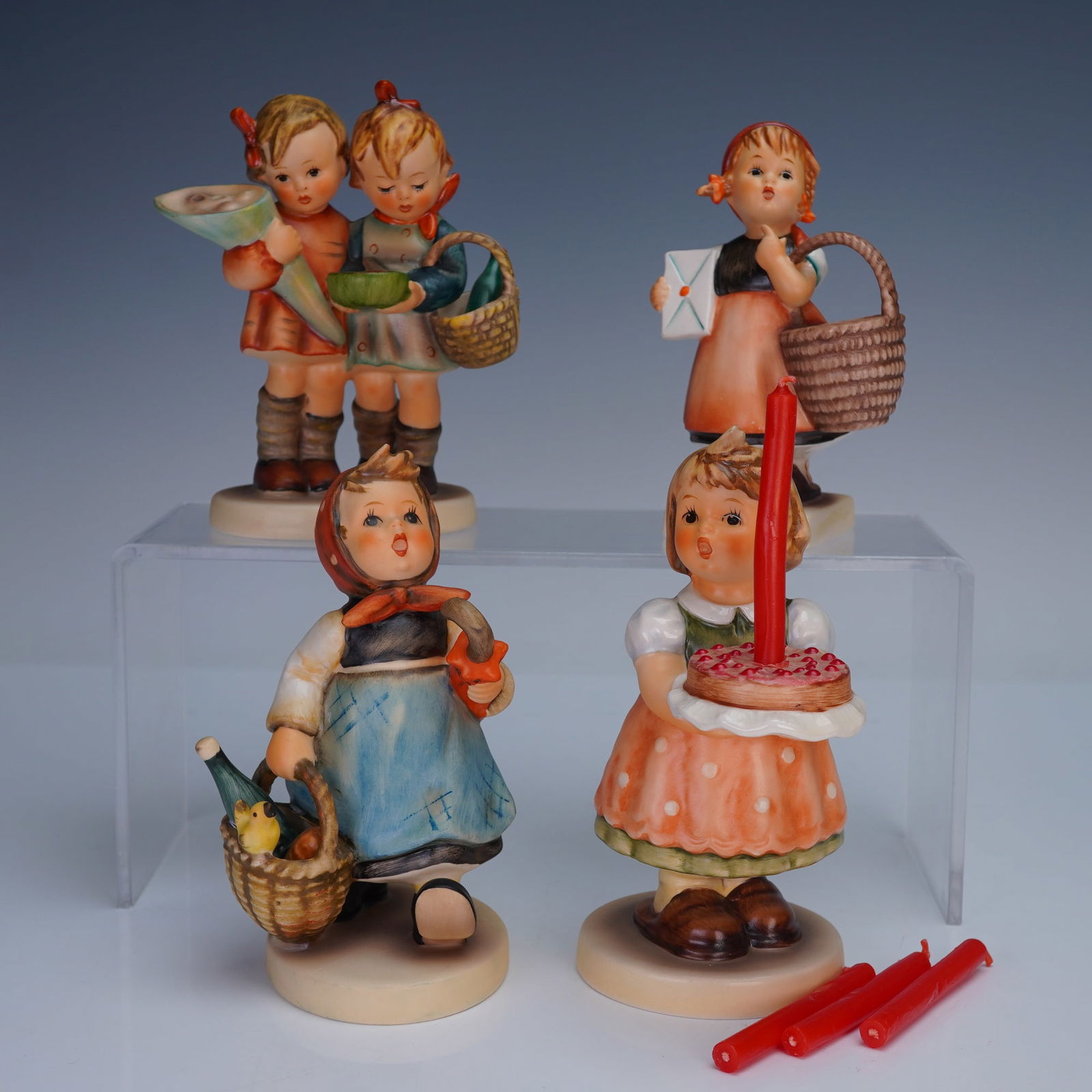 4pc Goebel Hummel Figurines: Group of four vintage Goebel Hummel figurines including a girl with cake and red candles, a girl with basket and bottle, a girl with letter and basket, and two children with school supplies. Each piec