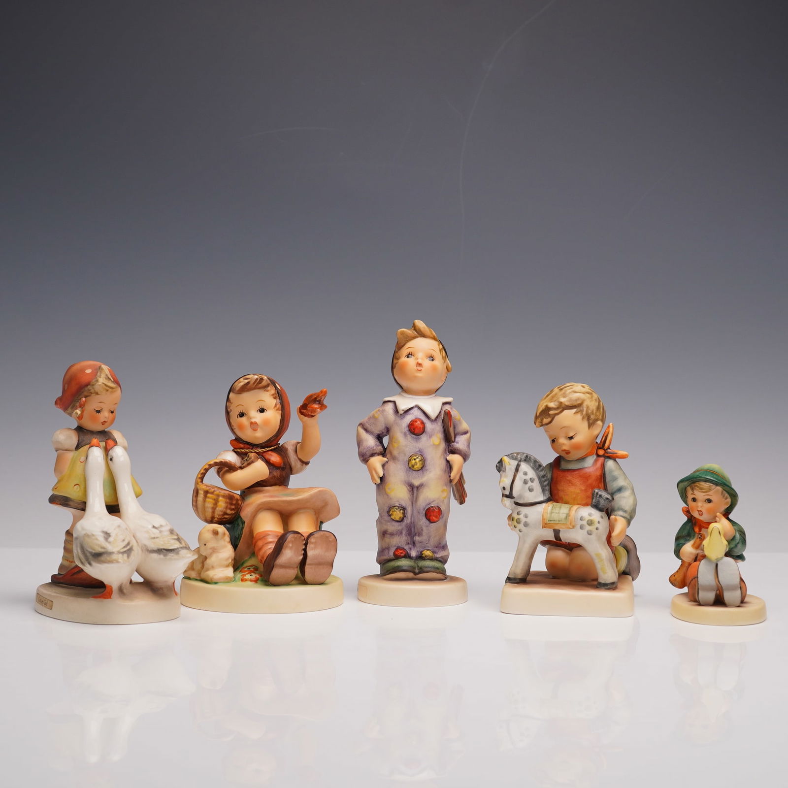 5pc Goebel Hummel Porcelain Figurines: Five hand painted porcelain figurines, rendered with charming detail, depicting children in various endearing poses. This selection includes Goose Girl, Carnival, Horse Trainer, Farewell, and Singing