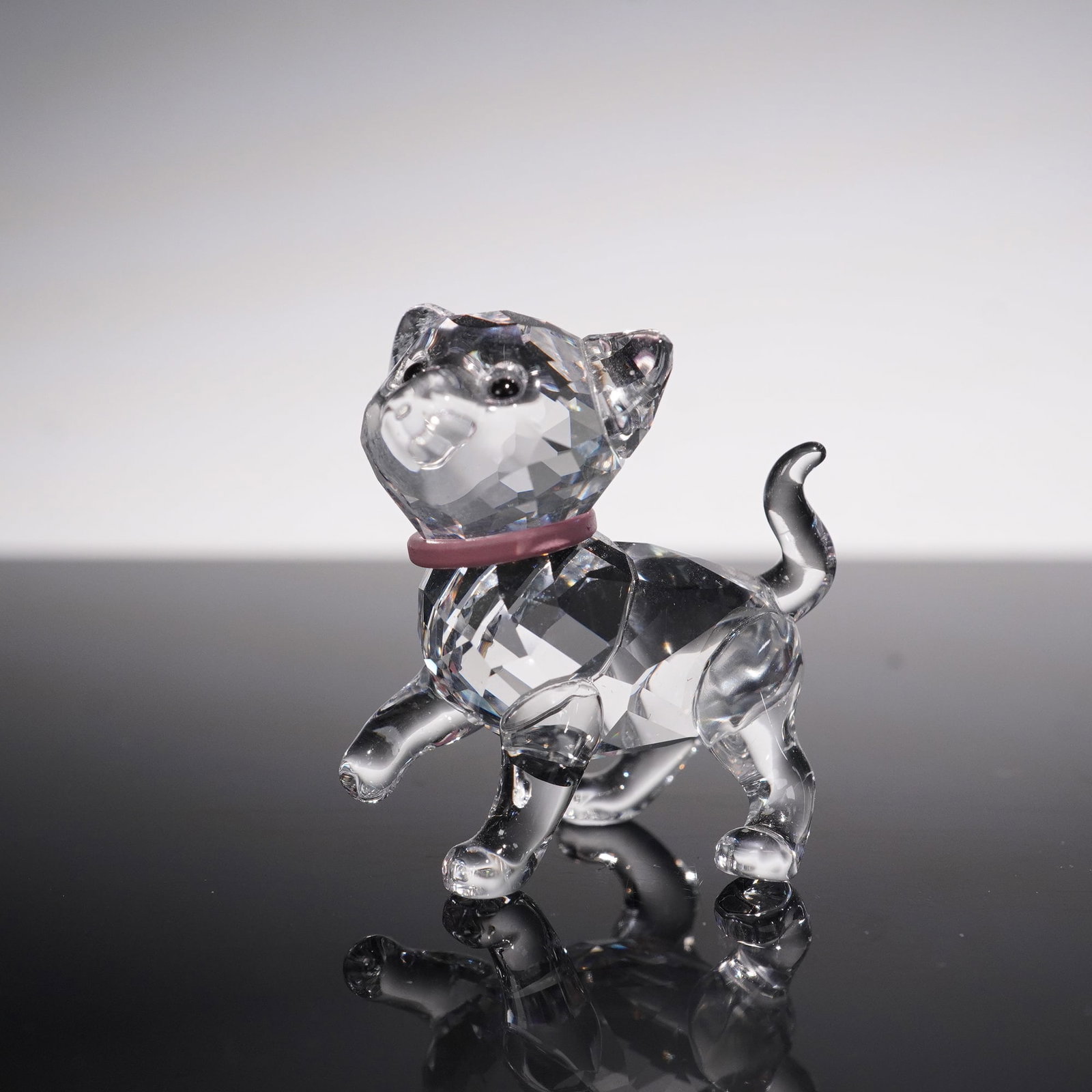Swarovski Crystal Figurine, Kitten with Pink Collar: Charming Swarovski crystal figurine depicting a playful kitten with a raised paw and curled tail, detailed with a pink crystal collar. Finely faceted clear crystal body captures and reflects the light