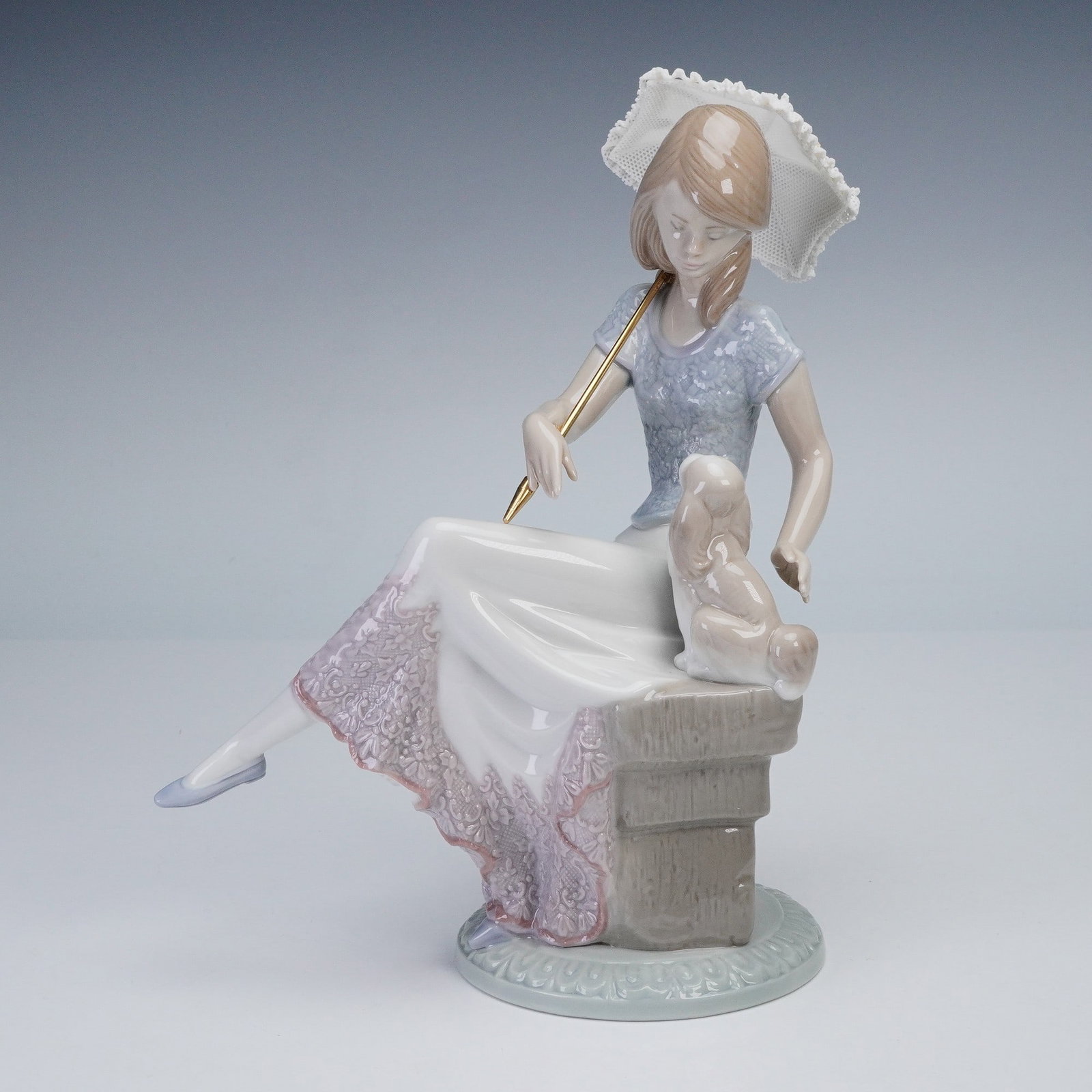 Lladro Porcelain Figurine Picture Perfect 01007612: Lladro porcelain figurine titled Picture Perfect, model number 01007612, depicts a young woman seated with a parasol resting on her shoulder as she gazes down at a playful puppy at her side. The figur