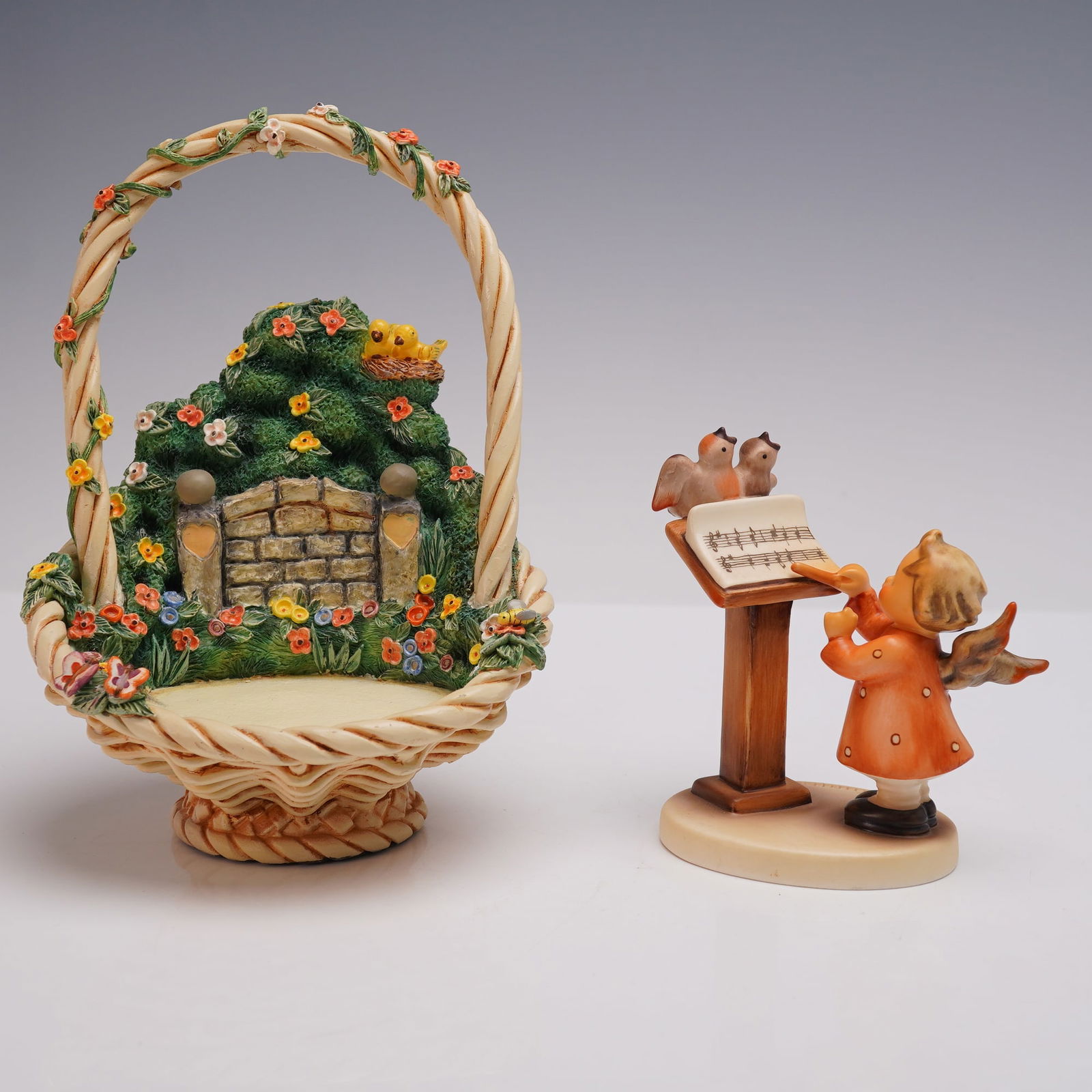 2pc Goebel Hummel Celestial Harmony Set: Goebel Hummel figurine Bird Duet Hum 169 depicting an angel in orange coat conducting birds at a music stand, together with the HummelScapes Celestial Harmony basket display featuring a floral arch an