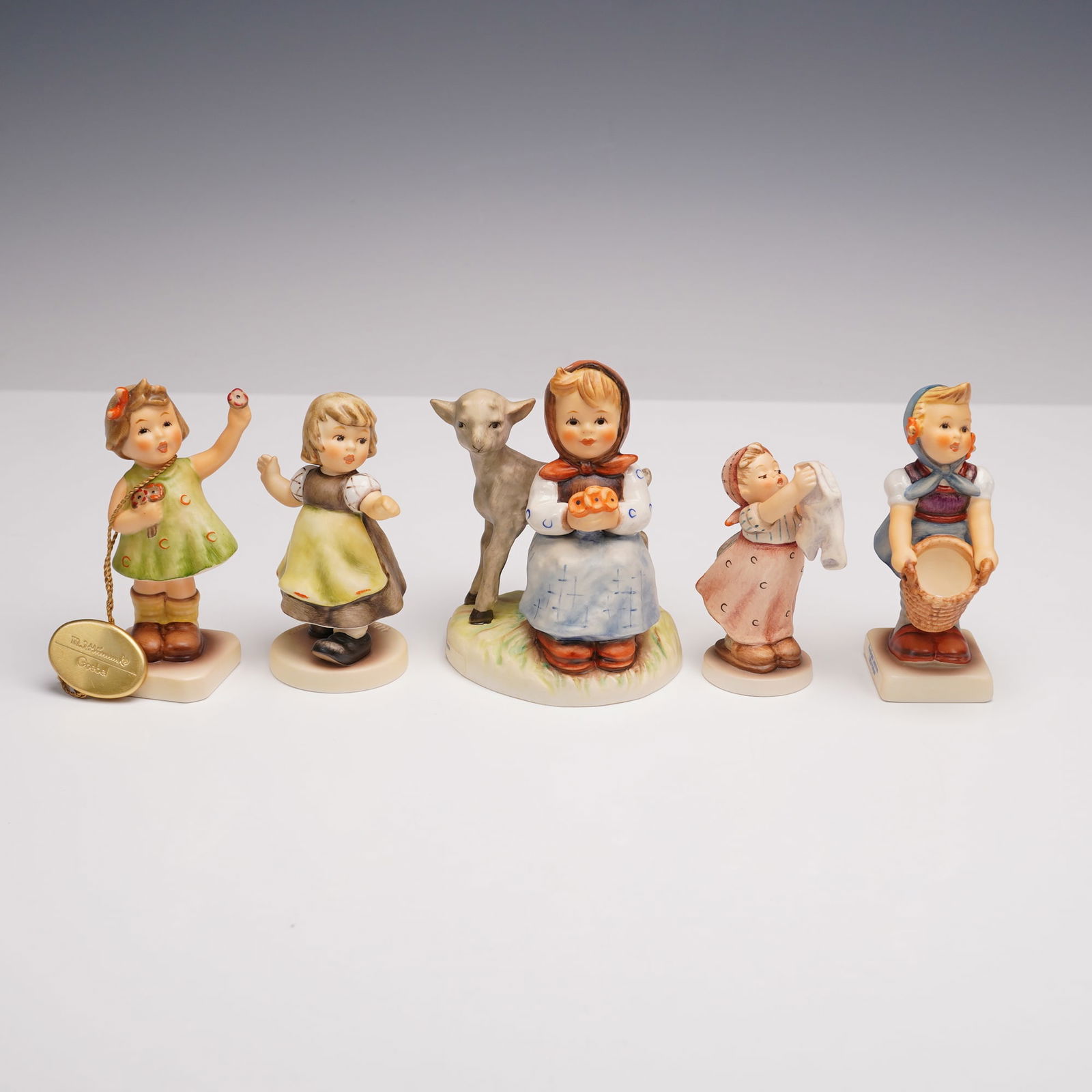 5pc Goebel Hummel Figurines- Girls at Play and Daily Tasks: Charming collection of five Goebel Hummel figurines featuring young girls engaged in playful and everyday activities. The lot includes Spring Waltz (912/B) depicting a girl joyfully dancing, Little He
