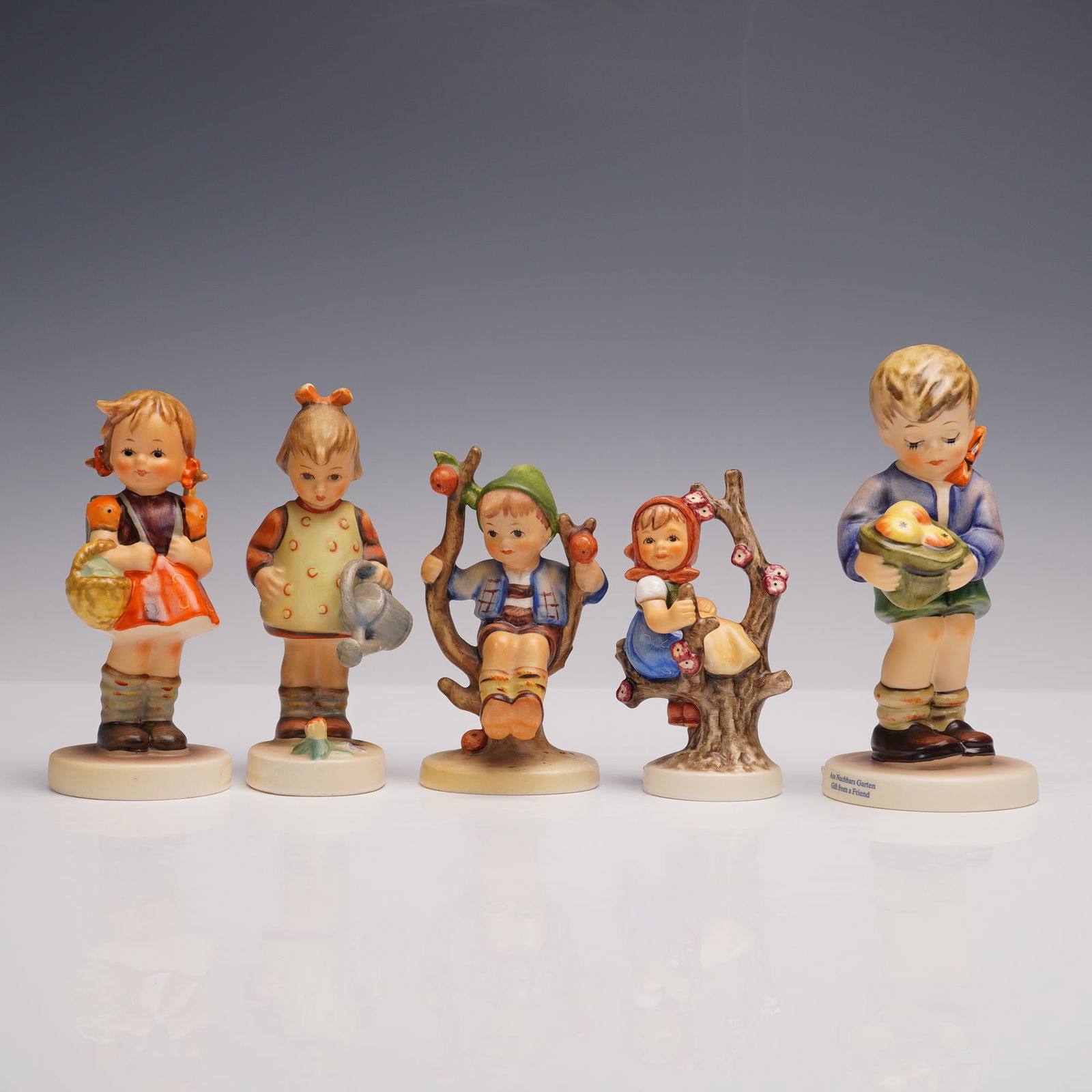5pc Goebel Hummel Porcelain Figurines: A lot of five porcelain figures, each hand-painted and depicting children in seasonal or pastoral settings. The group includes Apple Tree Girl, Apple Tree Boy, Gift from a Friend, School Girl, and Lit