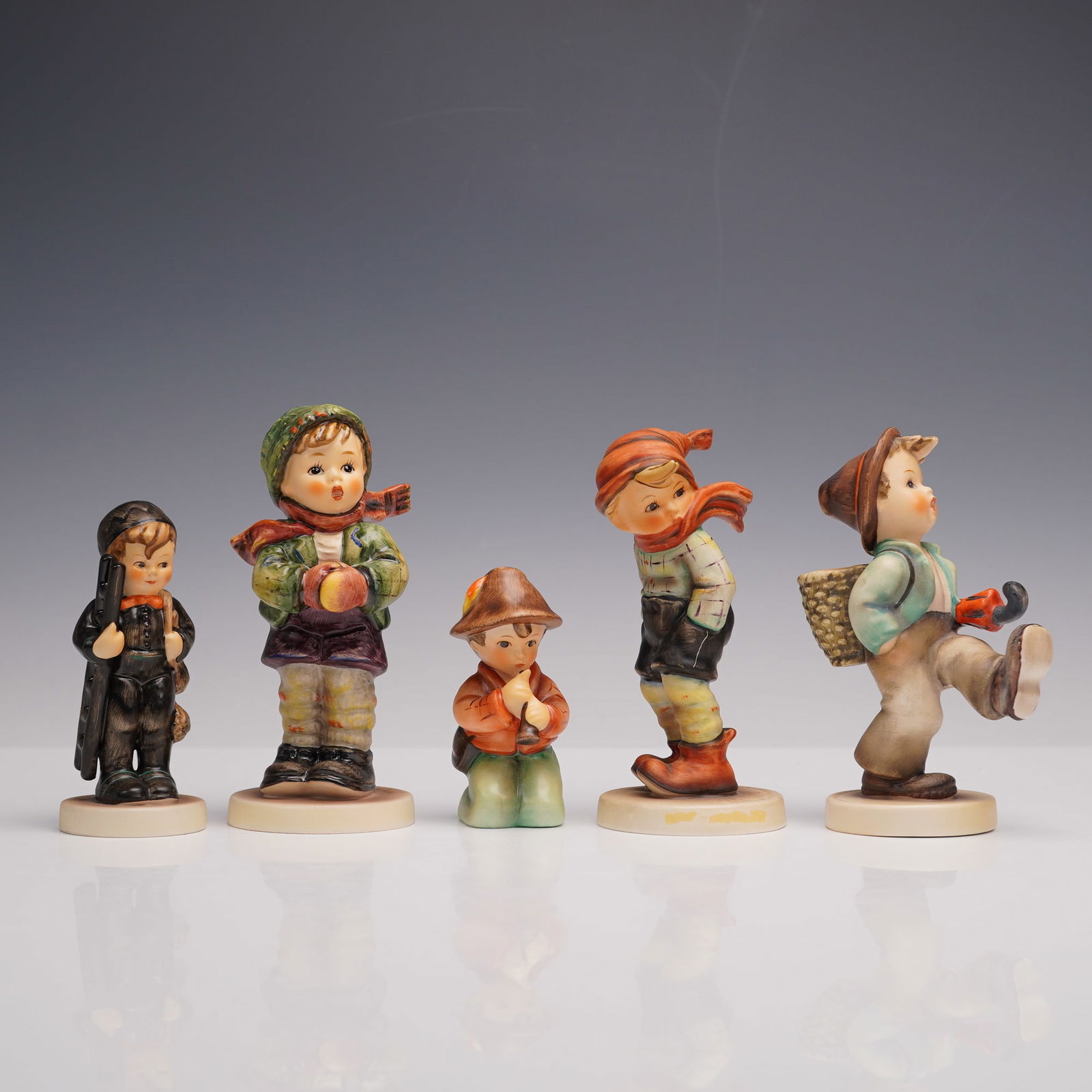 5pc Goebel Hummel Porcelain Figurines: A set of five hand painted figures depicting young boys in various poses. The group includes Little Tooter, Its Cold, Chimney Sweep, March Winds, and Globe Trotter. Depicted different activities such