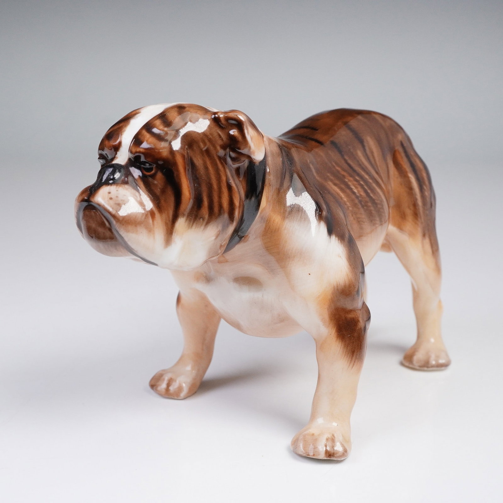 Royal Doulton Dog Figurine Bulldog HN1047: Royal Doulton Bulldog HN1047 designed by Frederick Daws. This small figurine captures the strong stance and determined character of the bulldog in brown and white glaze. The bulldog has long been a sy