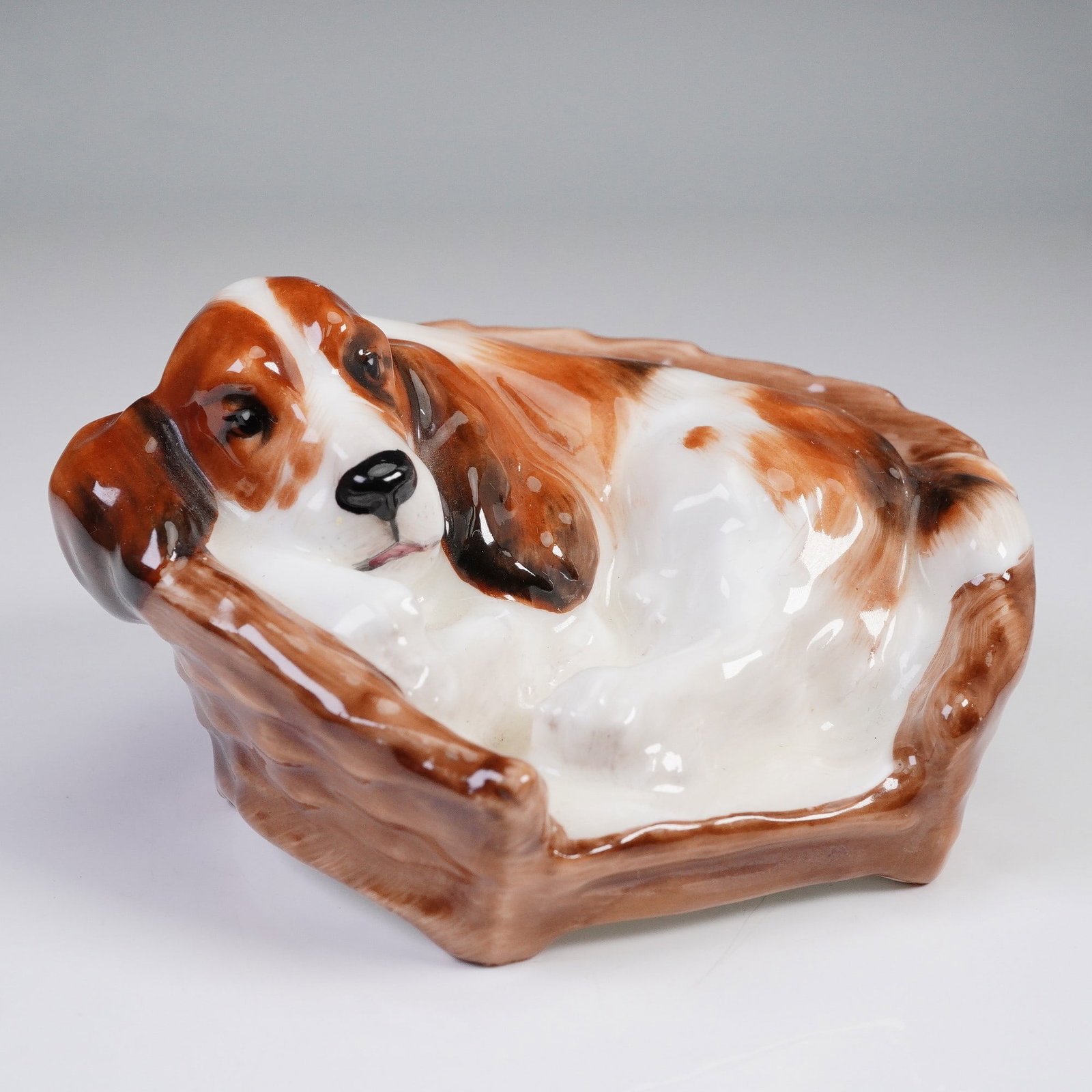 Royal Doulton Figurine, Cocker Spaniel HN2585: This delightful Royal Doulton figurine, model HN2585, portrays a resting cocker spaniel nestled comfortably in a woven basket. Finely crafted in bone china, the piece is hand-painted in warm tones of 