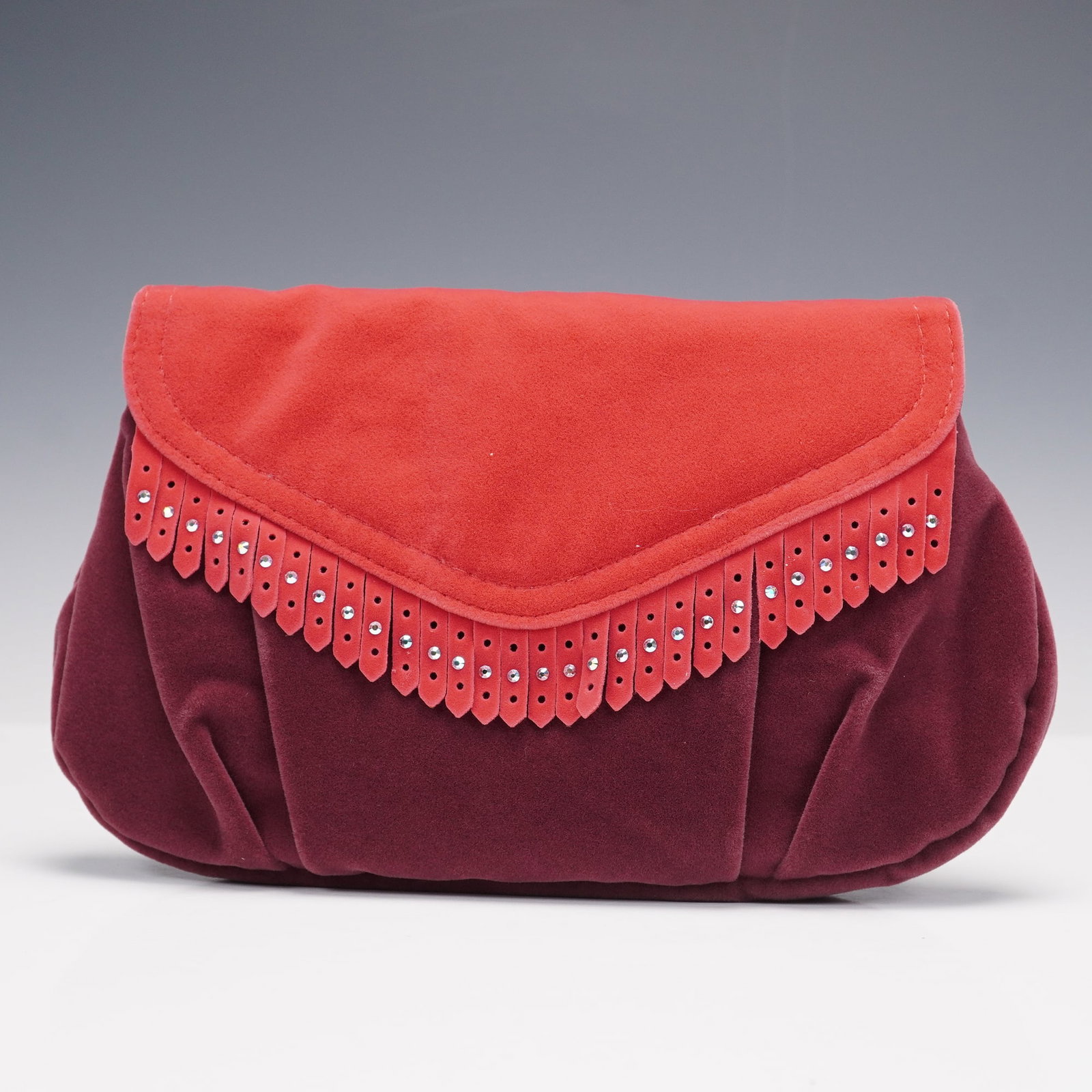 Swarovski Red Suede Clutch: This Swarovski clutch is crafted in deep red suede with a vibrant red flap accented by crystal detailing. The interior features a satin lining with a small mirror and an elastic pocket for essentials.