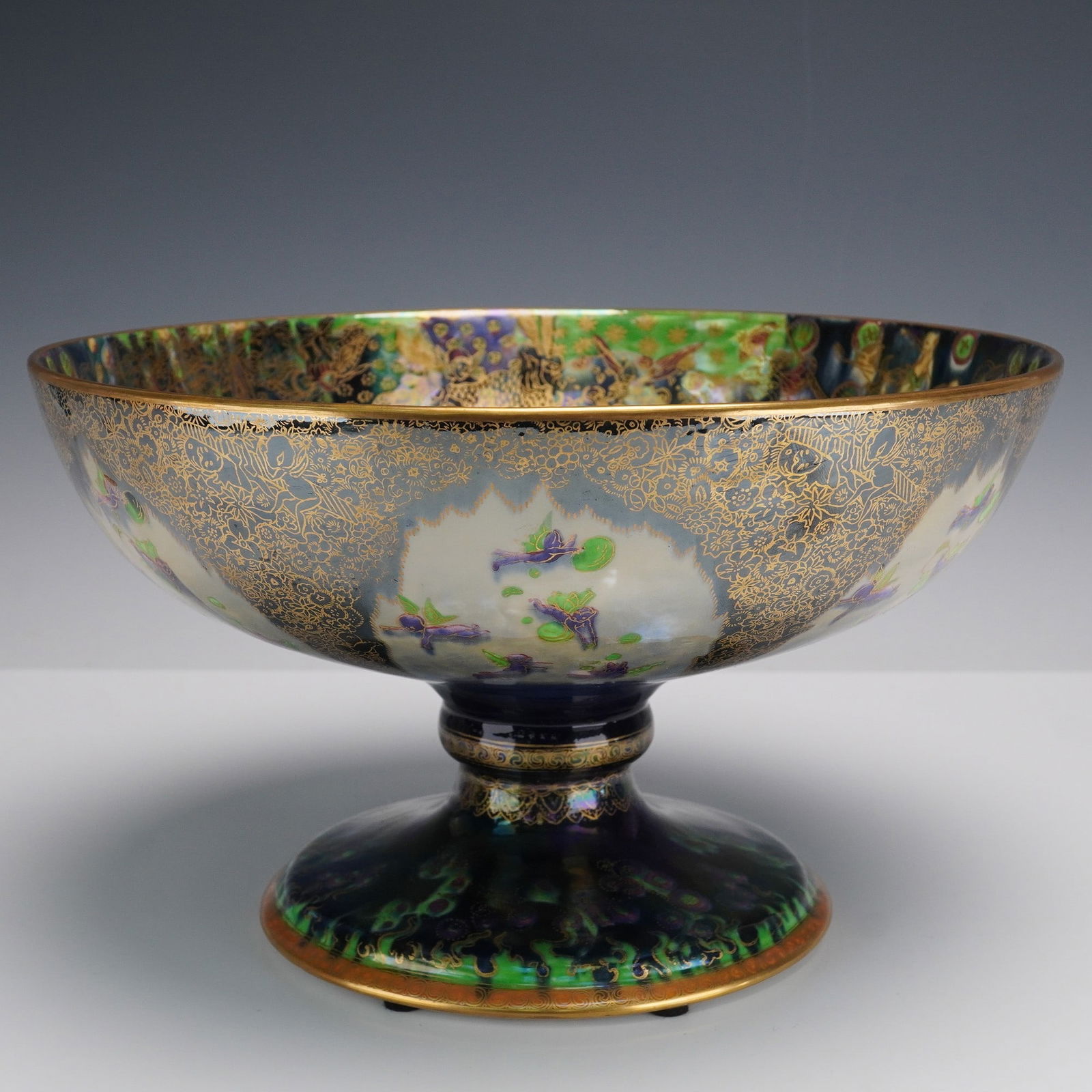 Wedgwood Fairyland Lustre Chalice Bowl, Twyford Garlands Z5360: The exterior features arch panels with baby fairies in violet, depicted flying and playing with green bubbles. The background shading transitions from white at the rim to deep blue, covered with grey