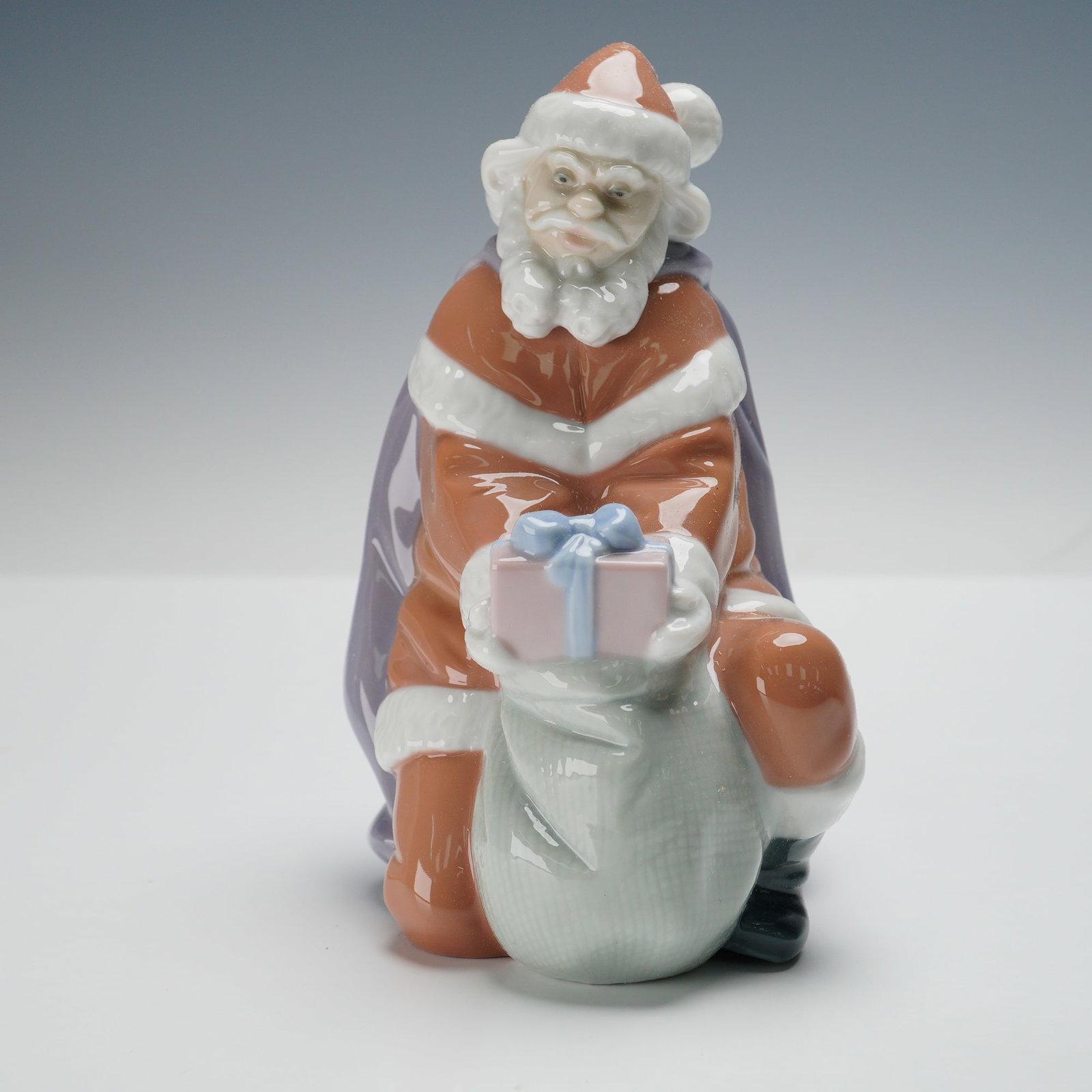 Lladro Porcelain Figurine, A Gift from Santa 01006575: Charming Lladro porcelain figurine titled A Gift from Santa (01006575), designed by Juan Huerta. This hand-painted figure portrays Santa Claus in his classic red suit, kneeling with a large gift sack 