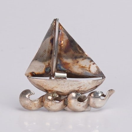 Sterling Silver Sailboat Brooch: Vintage sterling silver brooch in the form of a stylized sailboat with triangular sail above curling wave motifs, marked Sterling Denmark to reverse. The piece displays an attractive patina and is fit